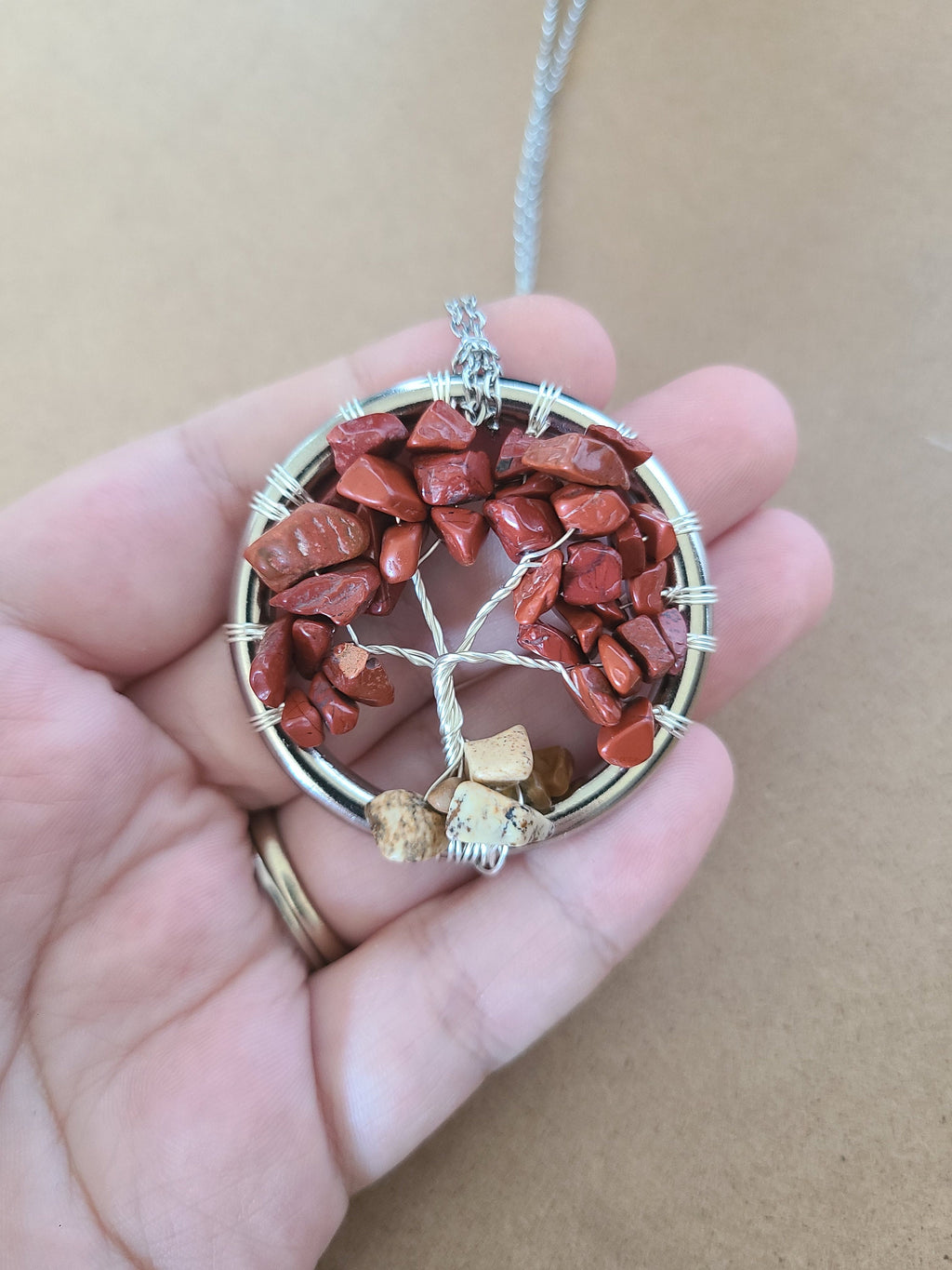 Tree-shaped pendant with red stones and silver wire on a hand against a beige background