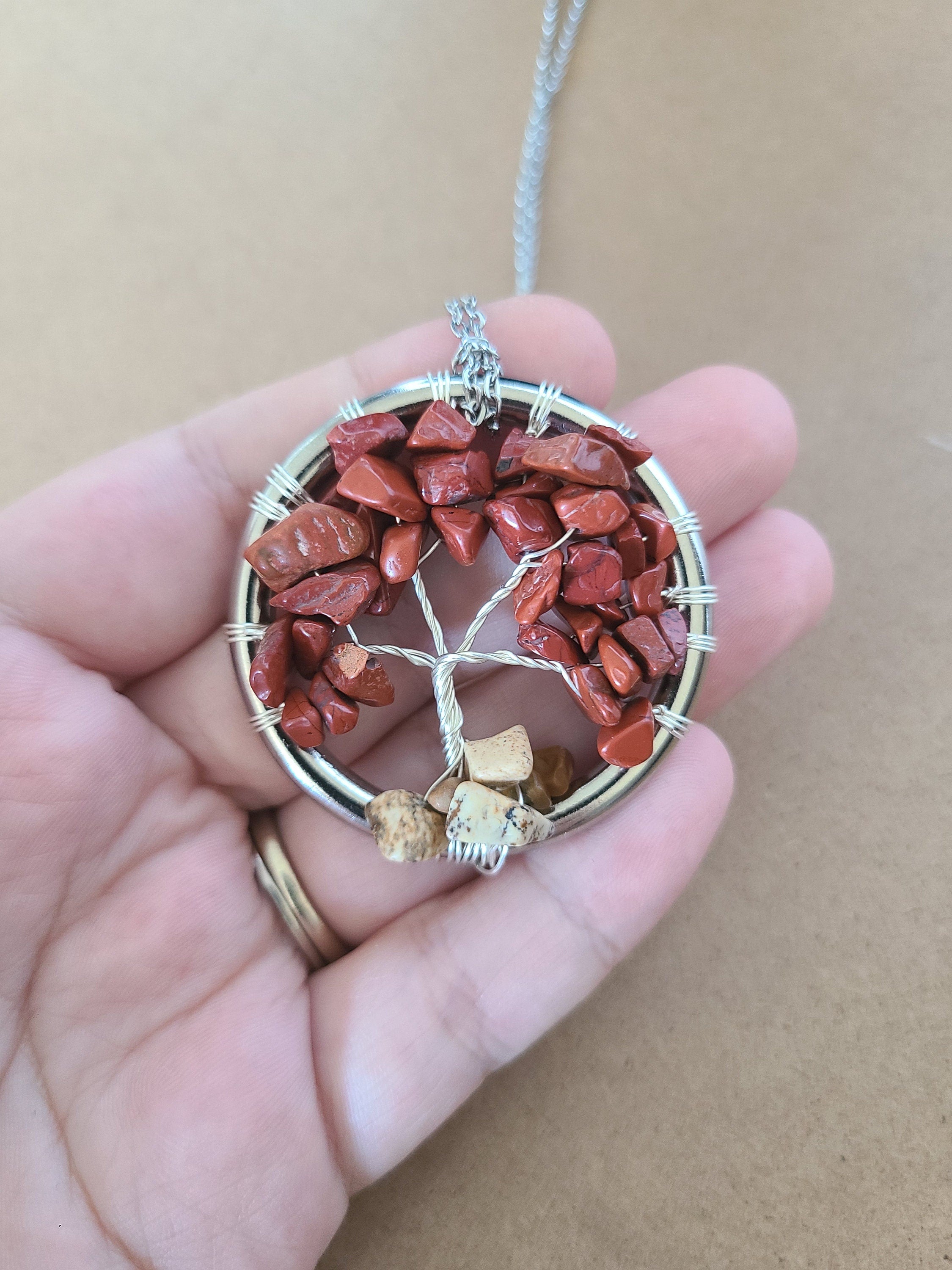 Tree-shaped pendant with red stones and silver wire on a hand against a beige background