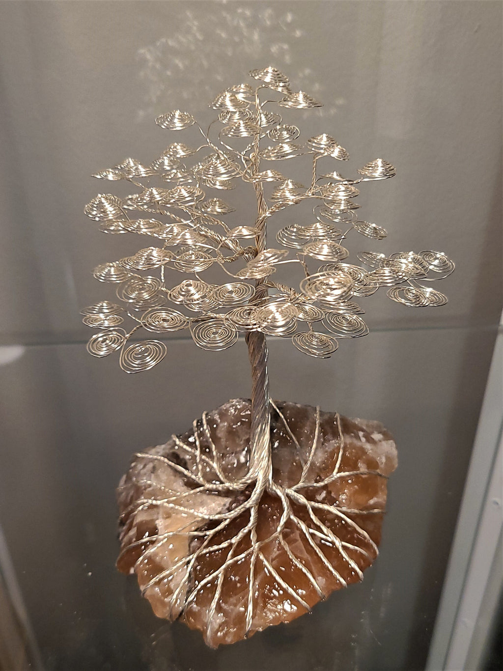 Decorative metal tree sculpture on a stone base against a neutral background