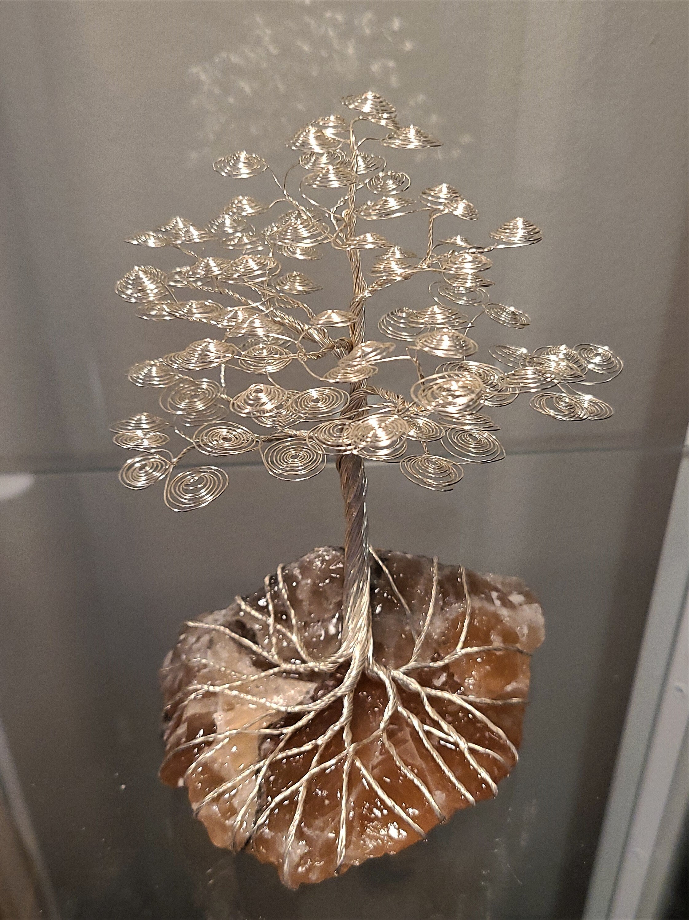 Decorative metal tree sculpture on a stone base against a neutral background