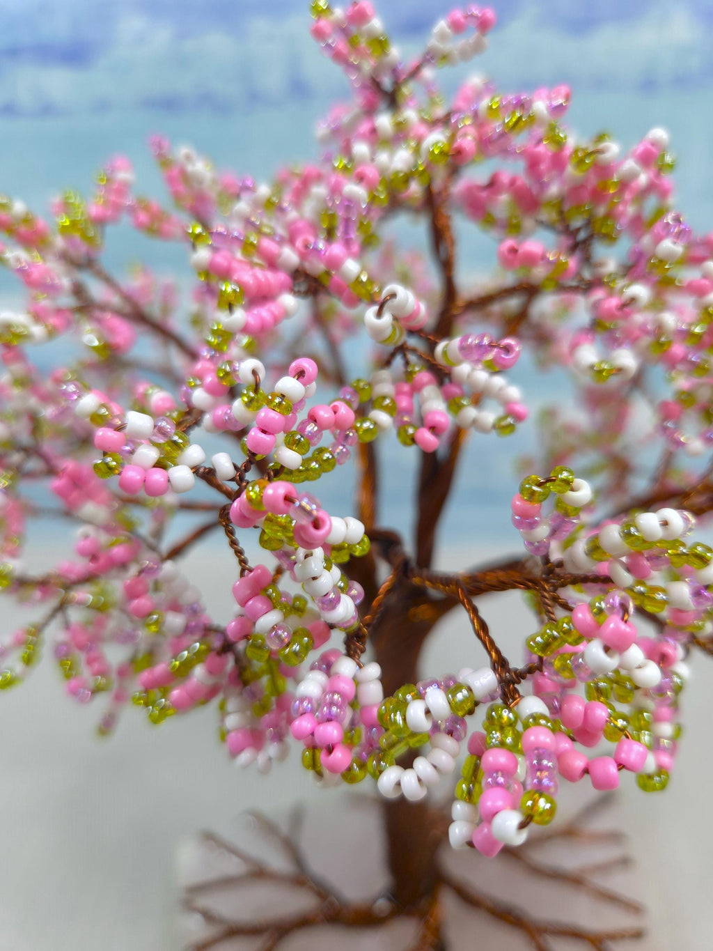 Decorative beaded tree with pink, white, and green beads against a blurred natural background