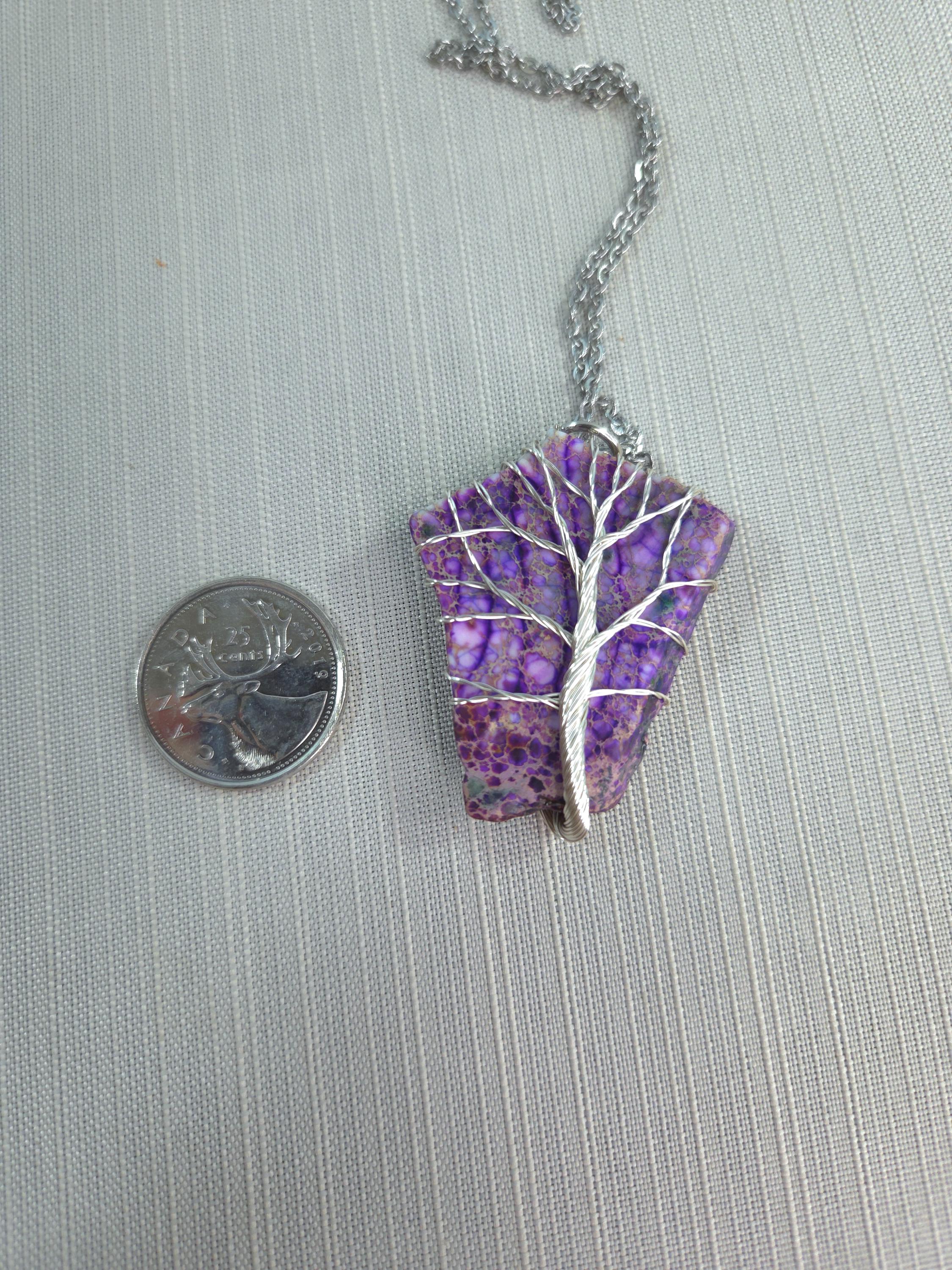 Purple stone pendant with silver tree design on a chain, next to a quarter for scale, on a gray background.