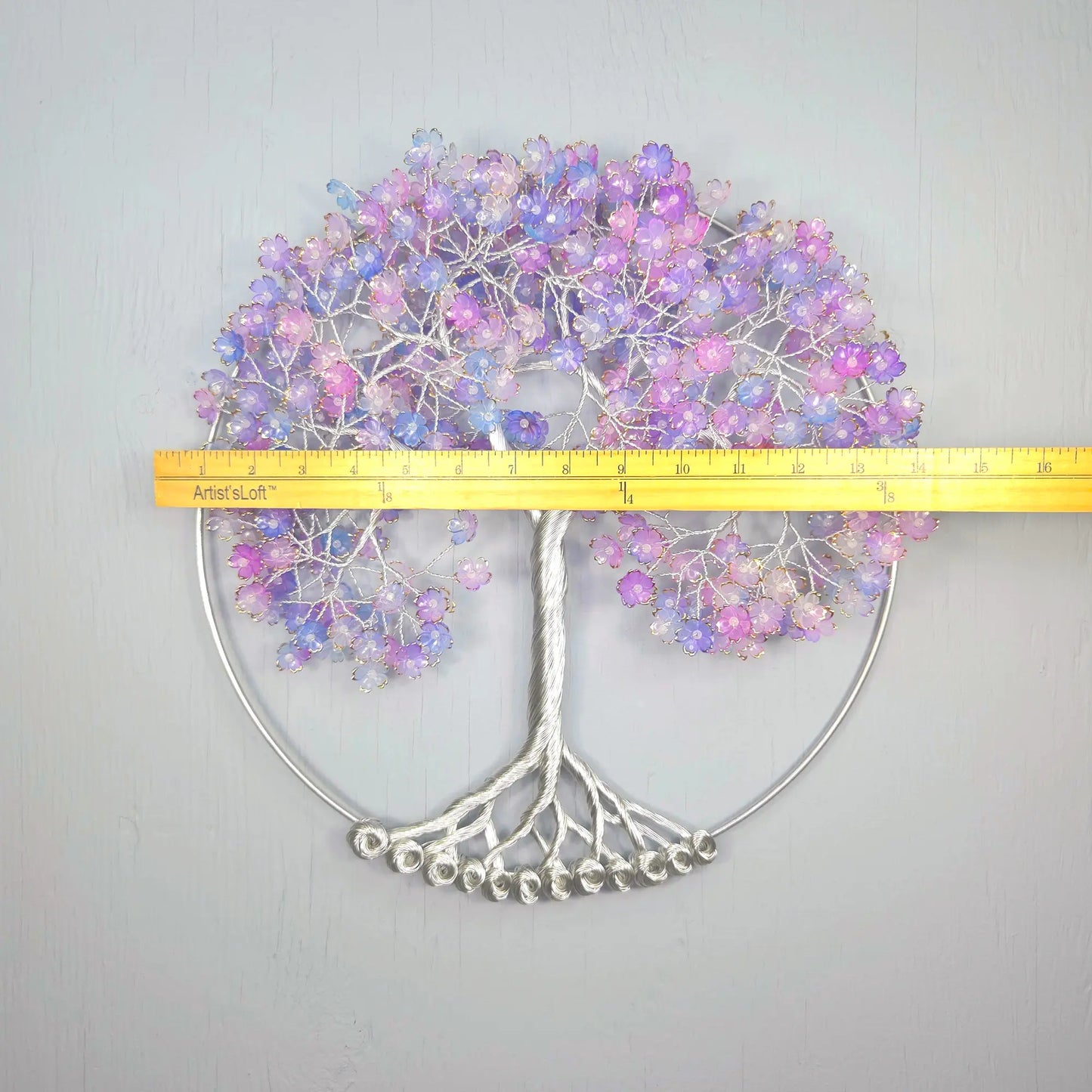 Decorative wall art with a tree design and purple flowers, measured against a yellow ruler.