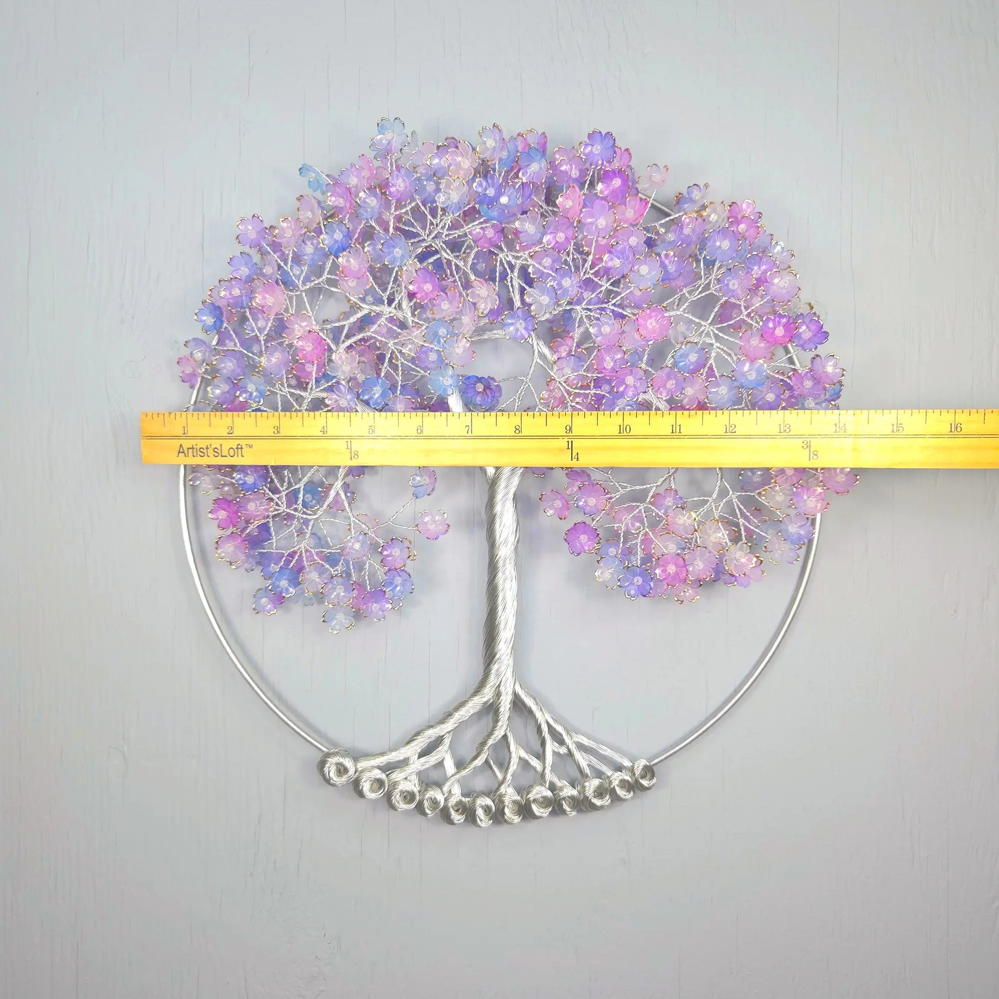 Decorative wall art with a tree design and purple flowers, measured against a yellow ruler.