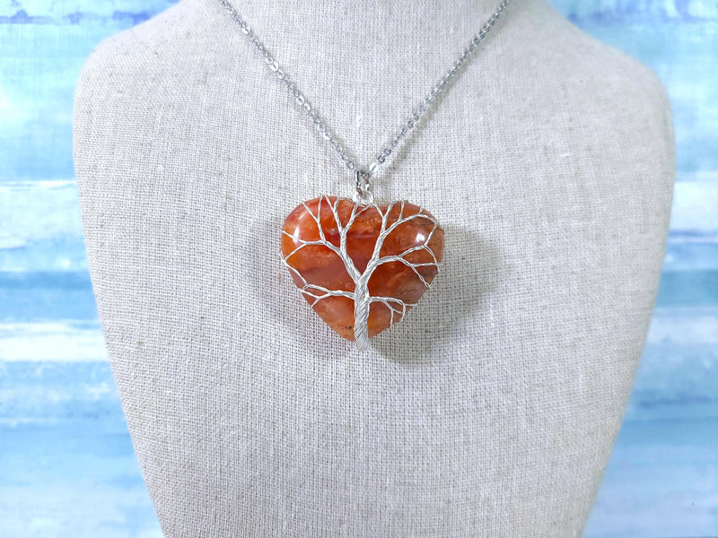 Necklace with a heart-shaped amber pendant on a mannequin bust against a blue and white striped background