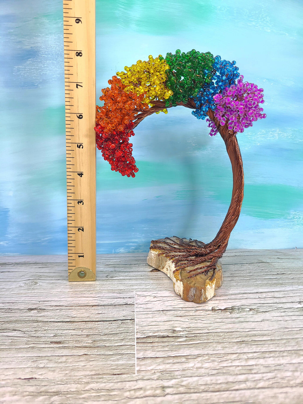 Colorful tree sculpture with rainbow leaves next to a ruler on a wooden surface