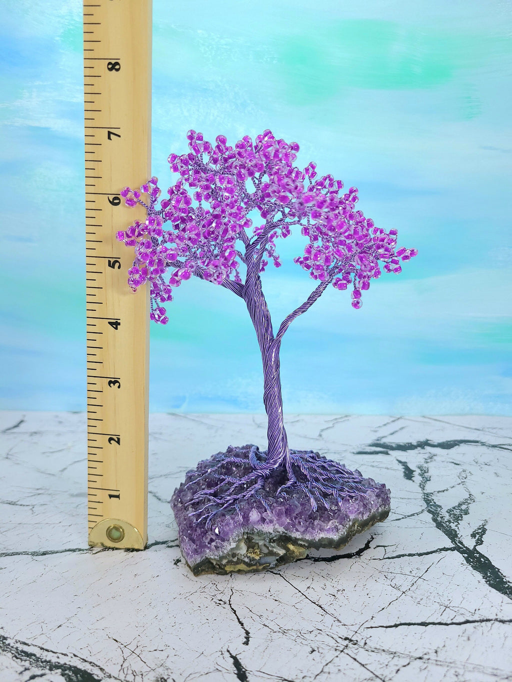 Small purple tree sculpture on a base with a ruler for scale against a blue gradient background