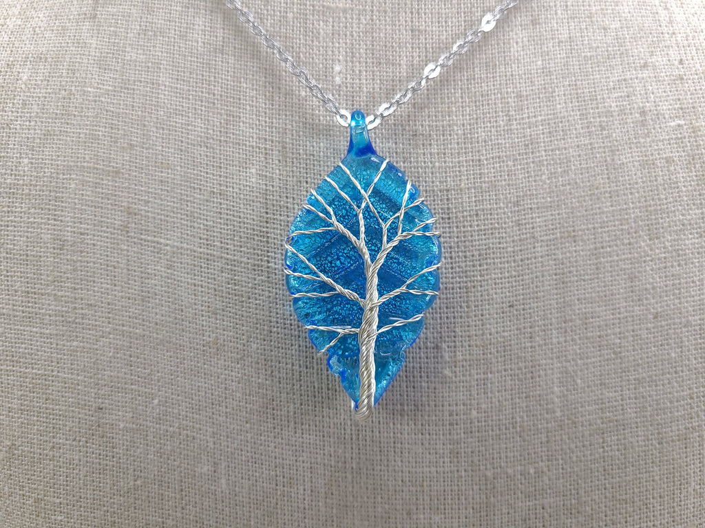 Blue leaf-shaped pendant with a tree design on a silver chain against a gray background
