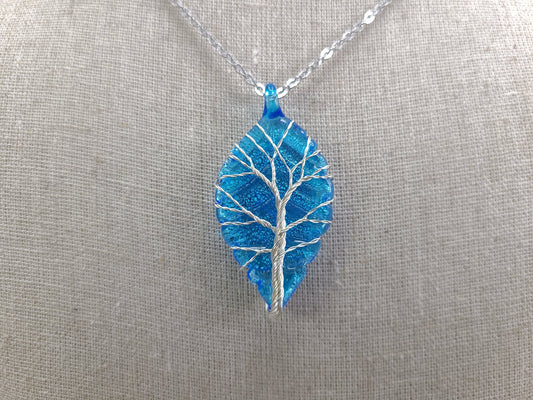 Blue leaf-shaped pendant with a tree design on a silver chain against a gray background