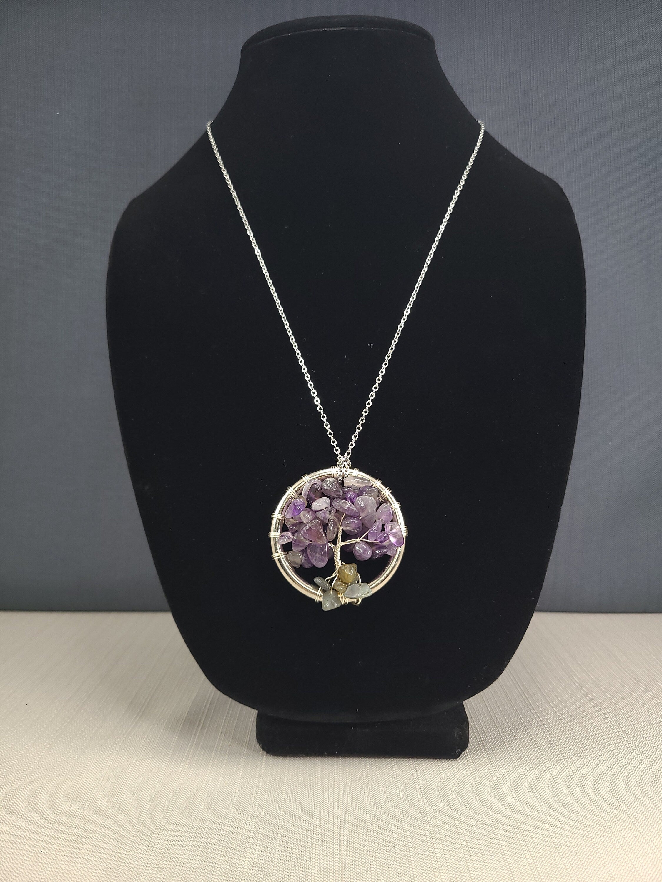 Necklace with a purple pendant on a black bust against a gray background