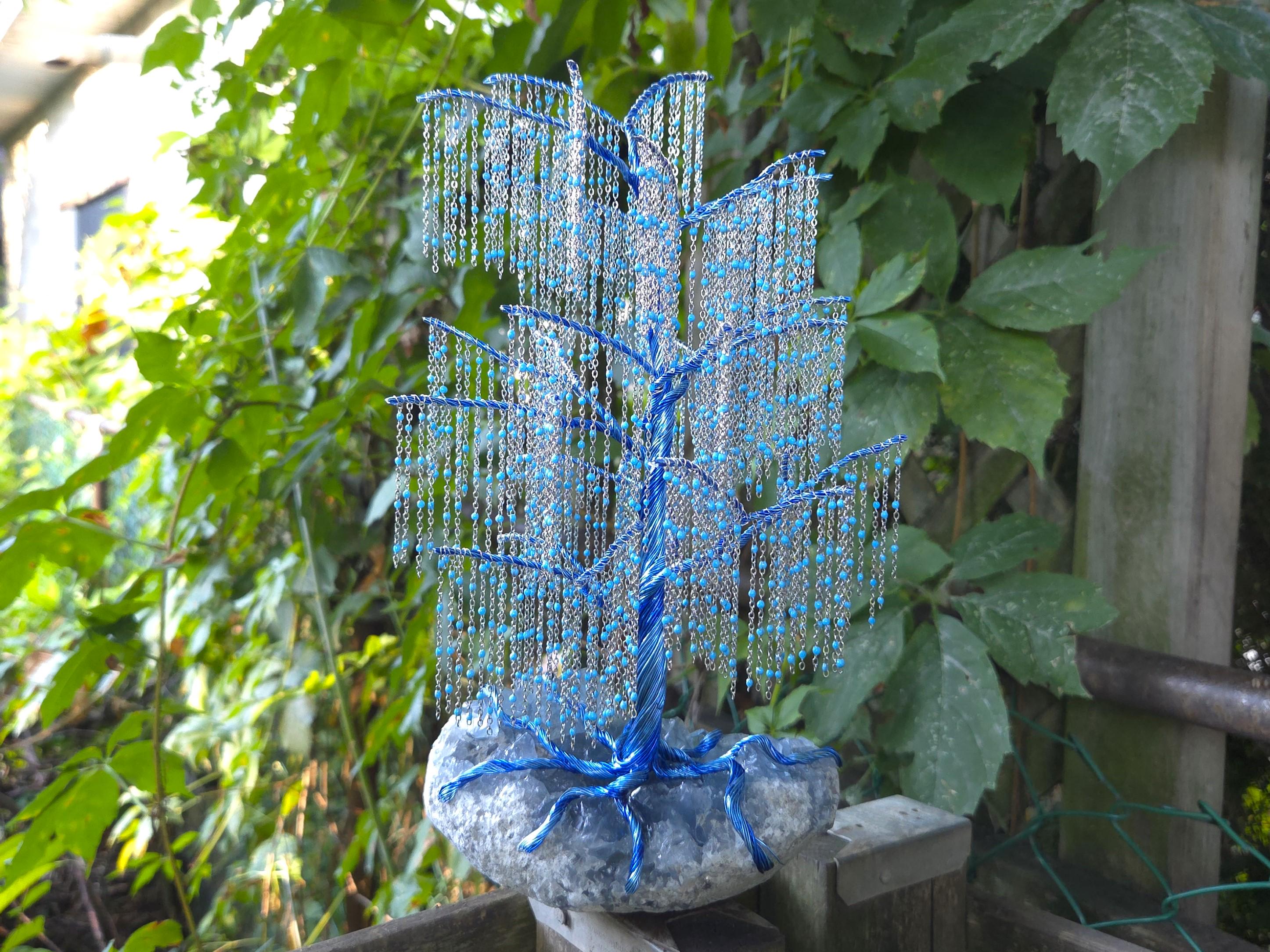 Decorative blue beaded tree sculpture against a natural green leafy background