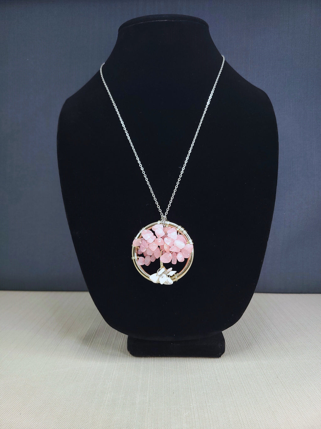 Necklace with a pink floral pendant on a black bust against a blue background