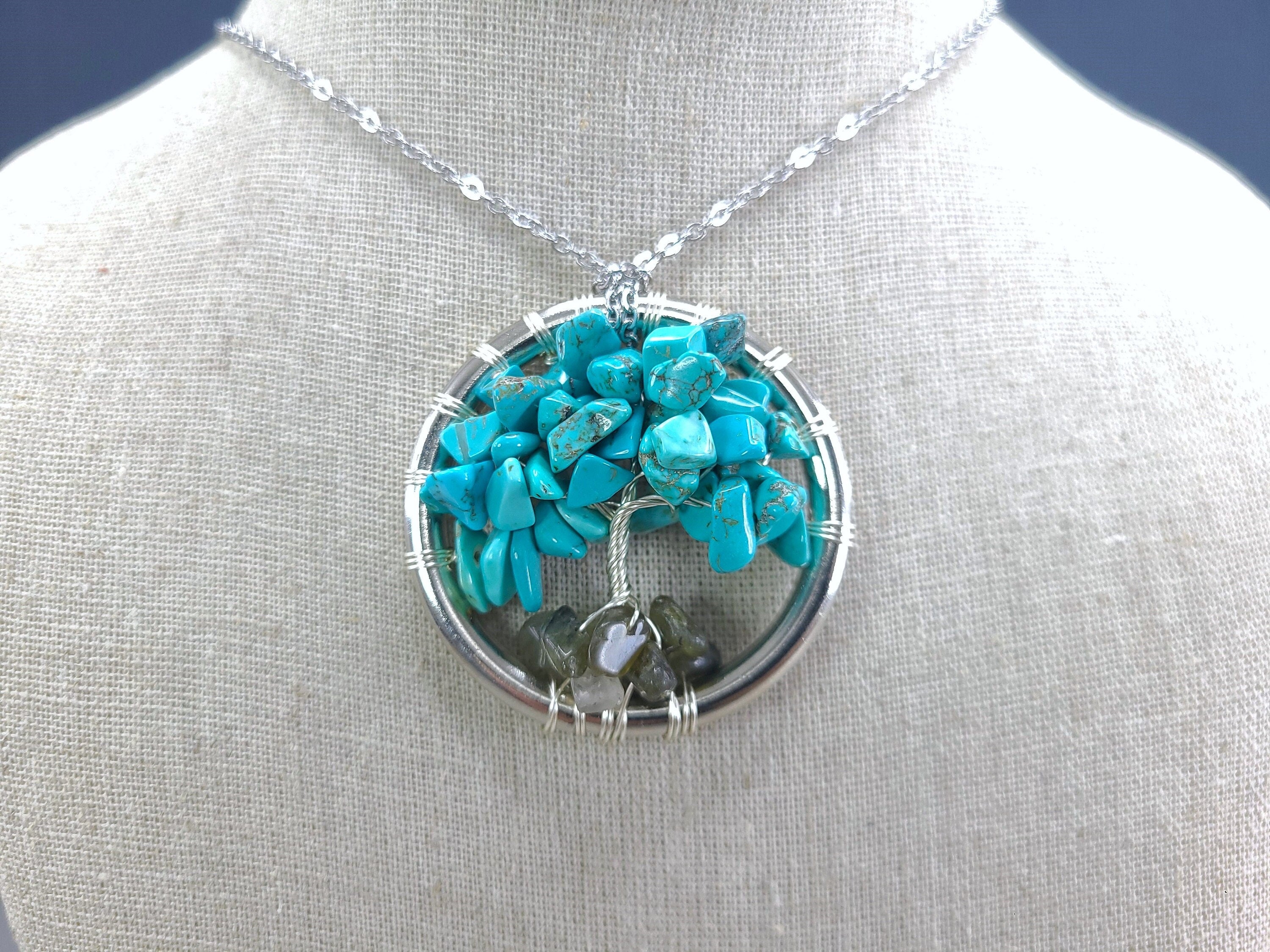 Turquoise stone tree of life pendant on a silver chain against a gray background