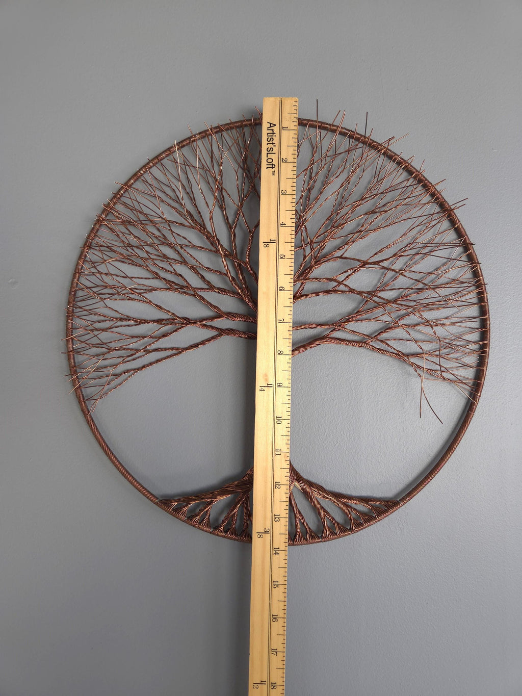 Decorative metal tree wall art with a ruler for scale on a gray background