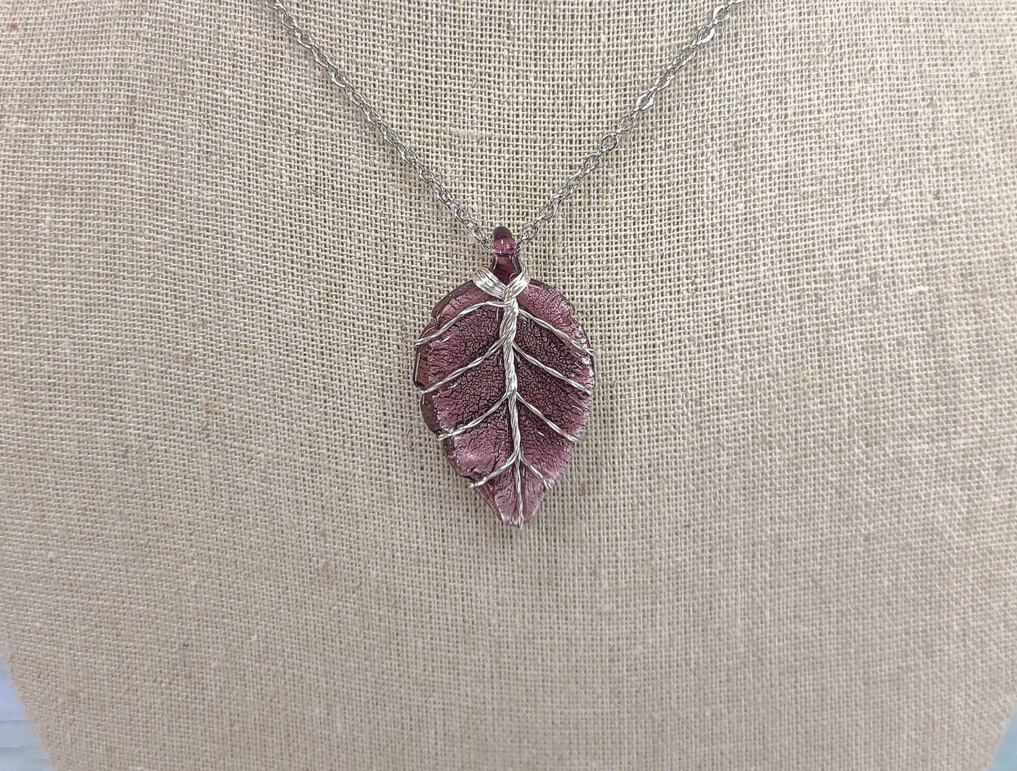 Purple leaf-shaped pendant on a chain against a beige fabric background