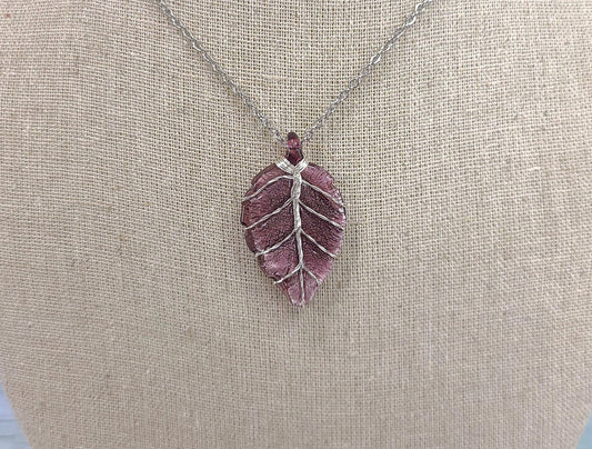 Purple leaf-shaped pendant on a chain against a beige fabric background