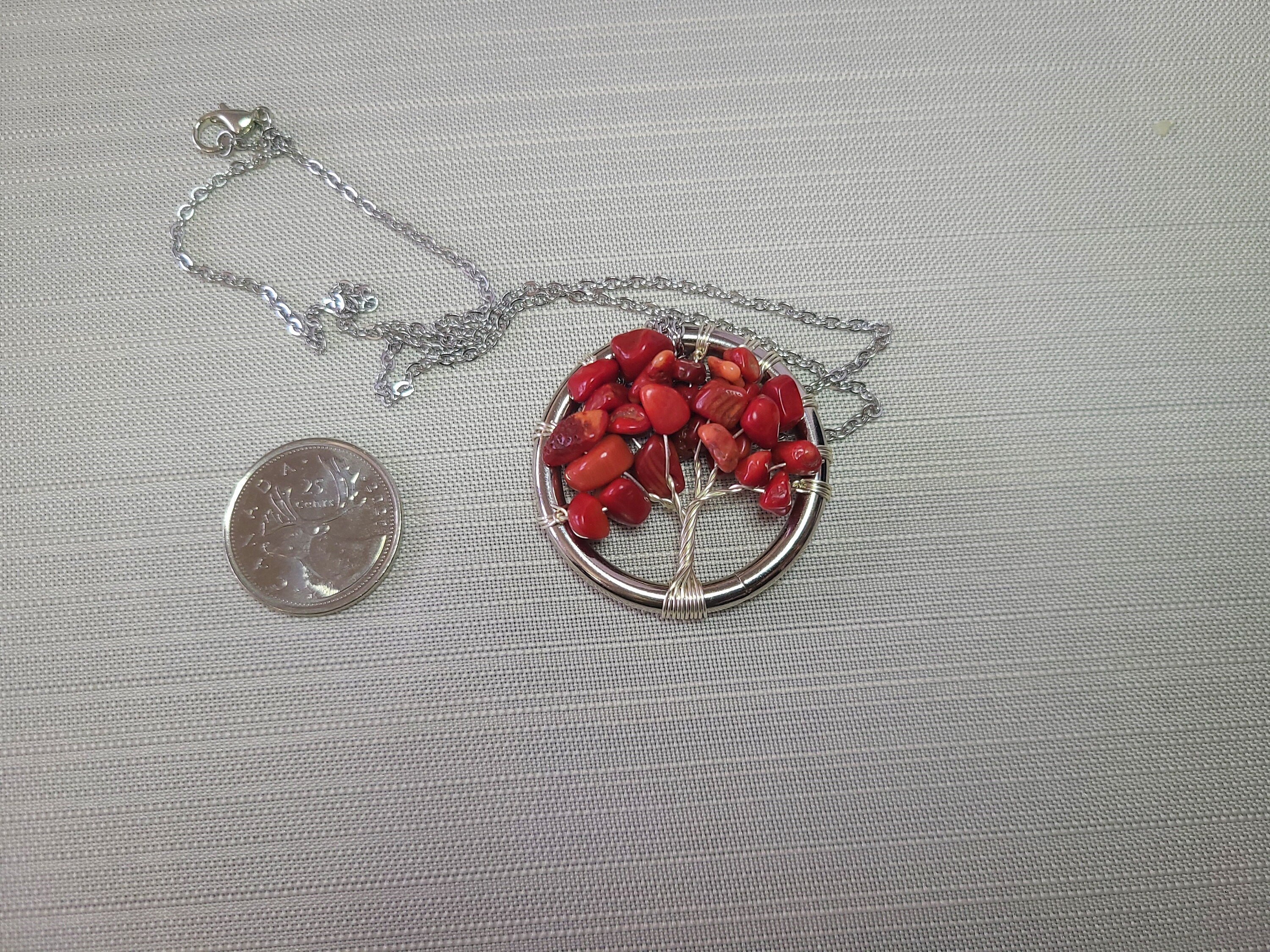 Necklace with red tree pendant next to a coin for scale on a gray background