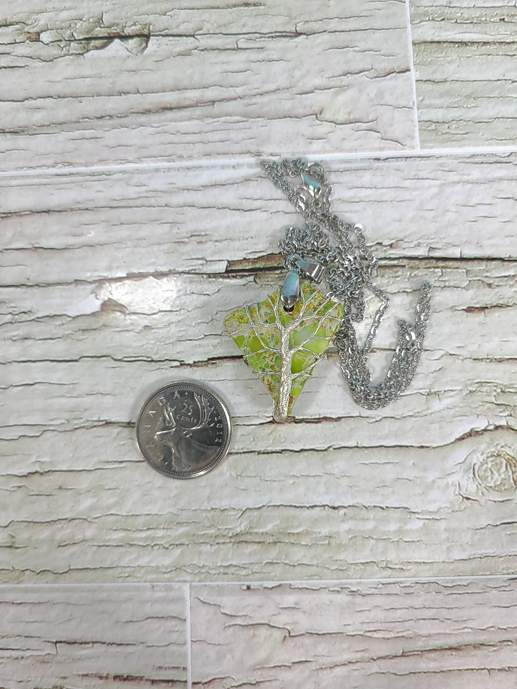 Necklace with a pendant on a wooden surface next to a coin for scale.
