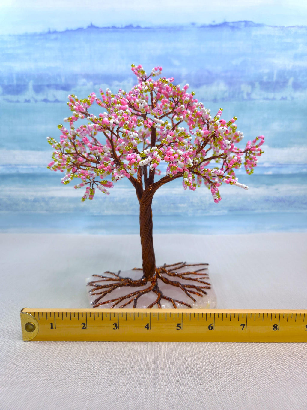 Model of a cherry blossom tree with pink flowers on a white surface, measured against a ruler.