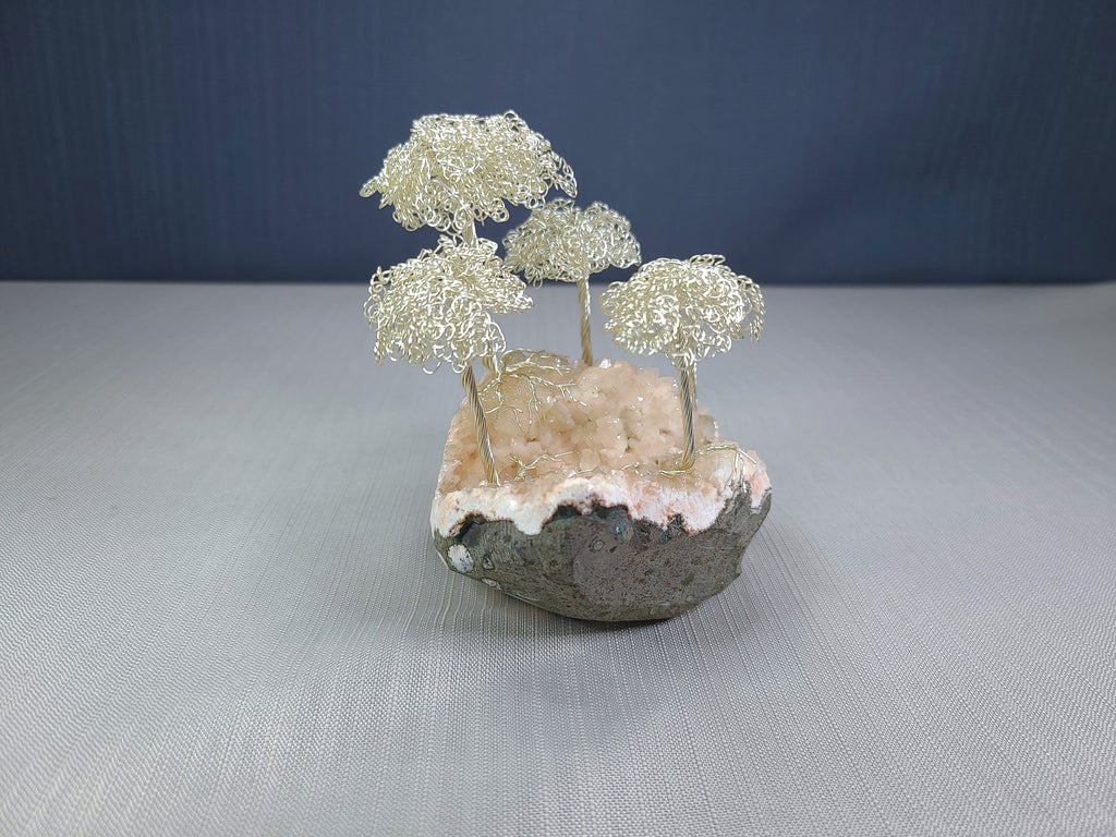 Small sculpture of wire trees on a rock base with a dark blue background