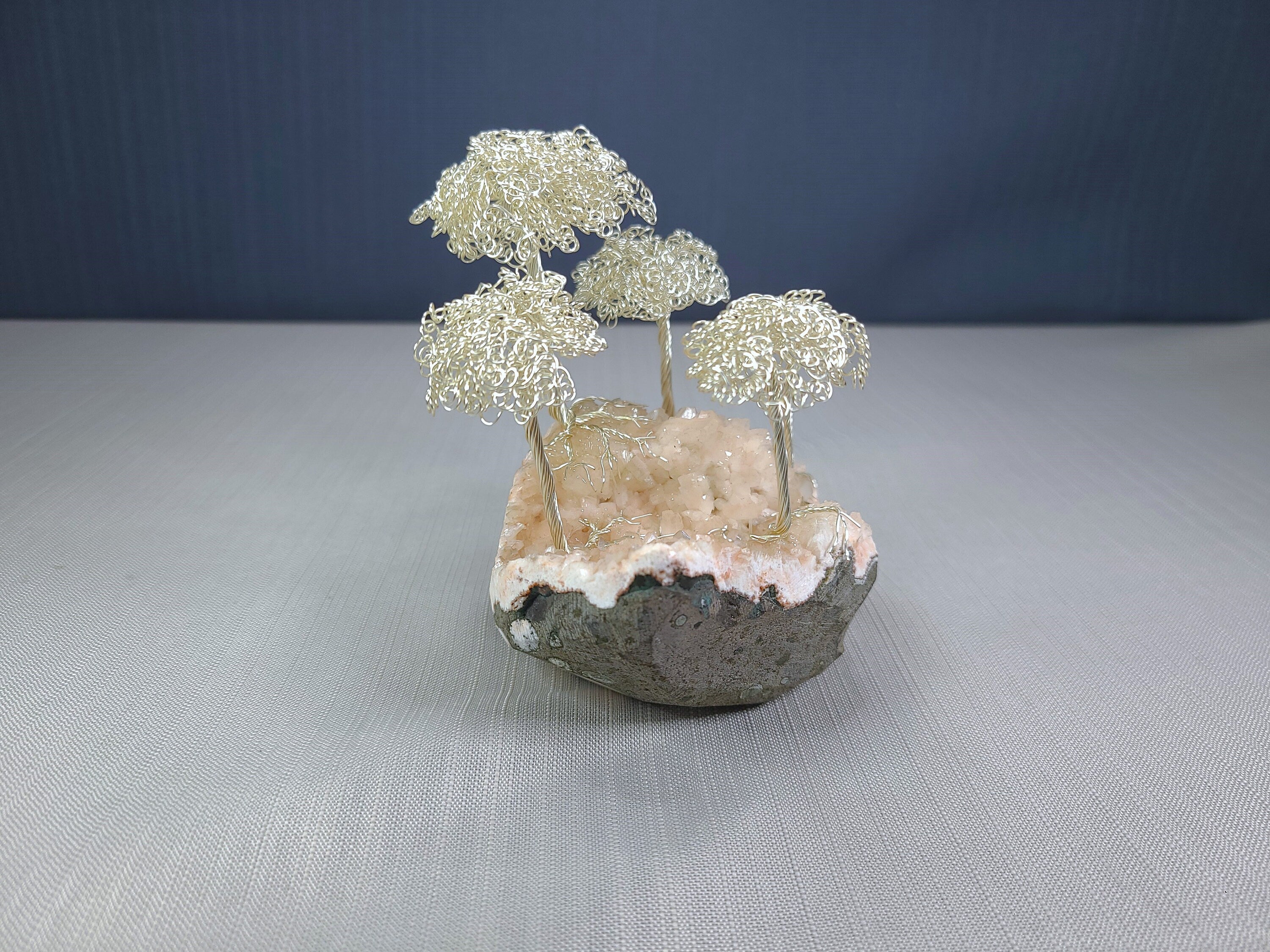 Small sculpture of wire trees on a rock base with a dark blue background