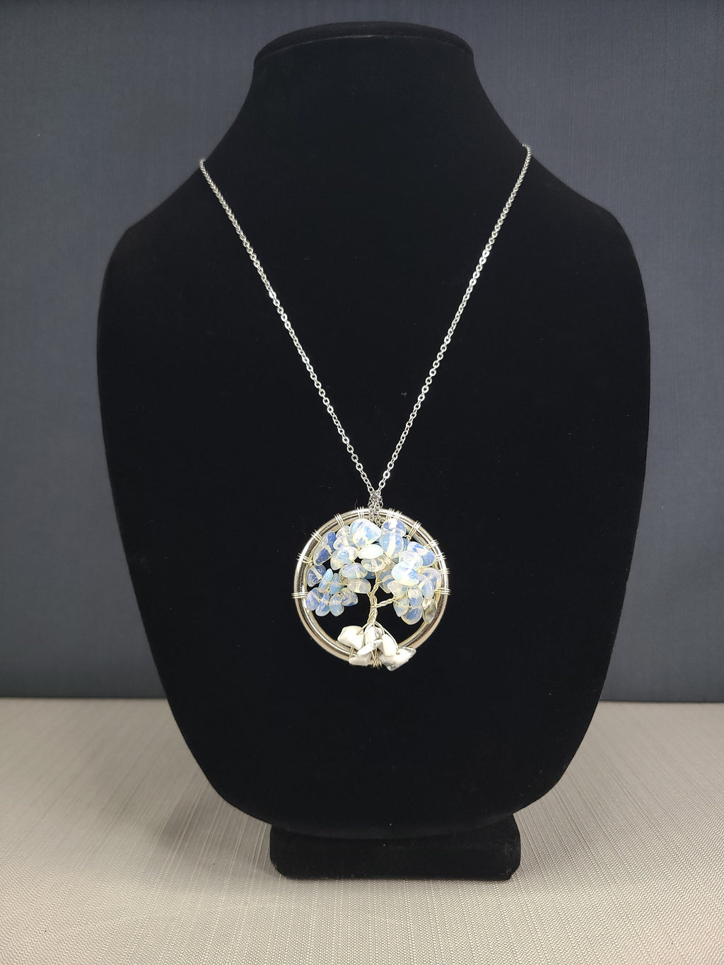 Necklace with a circular pendant on a black stand against a gray background