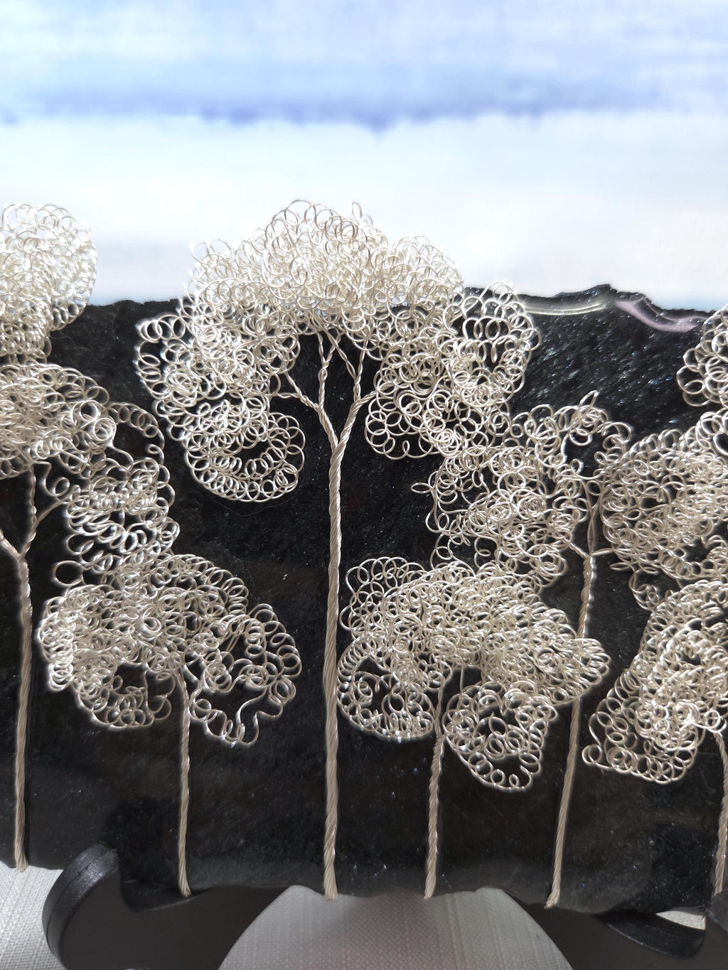 Decorative silver tree sculptures on a black background with a blue sky.