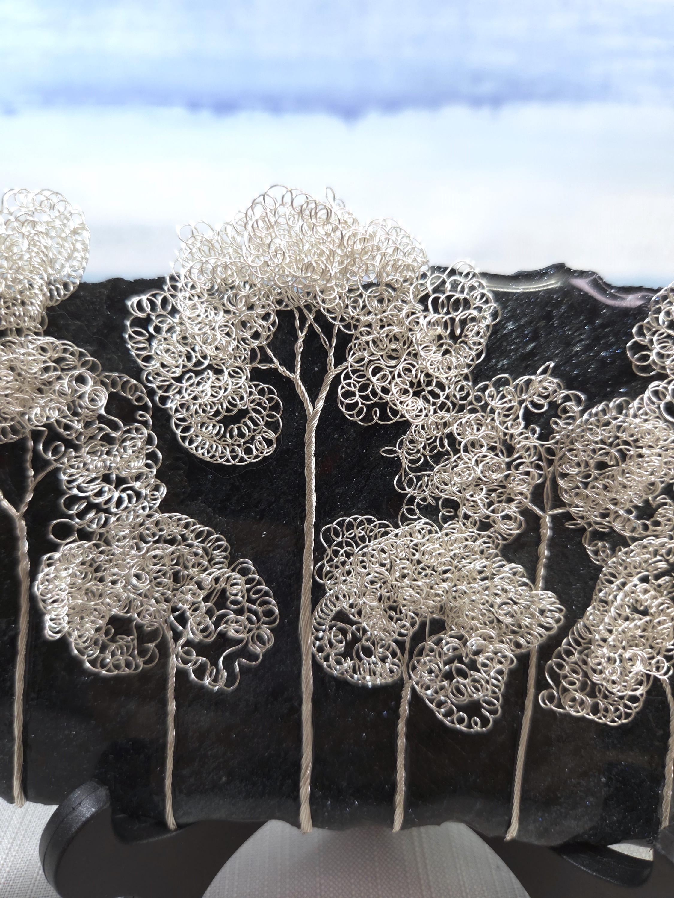 Decorative silver tree sculptures on a black background with a blue sky.