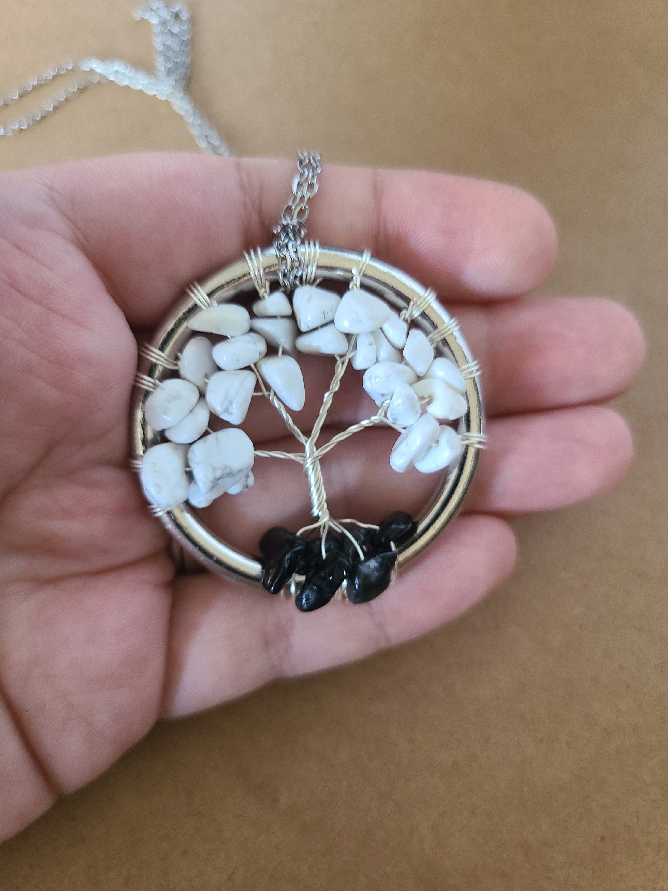 Tree of Life pendant with white stones and black accents held in a hand against a brown background