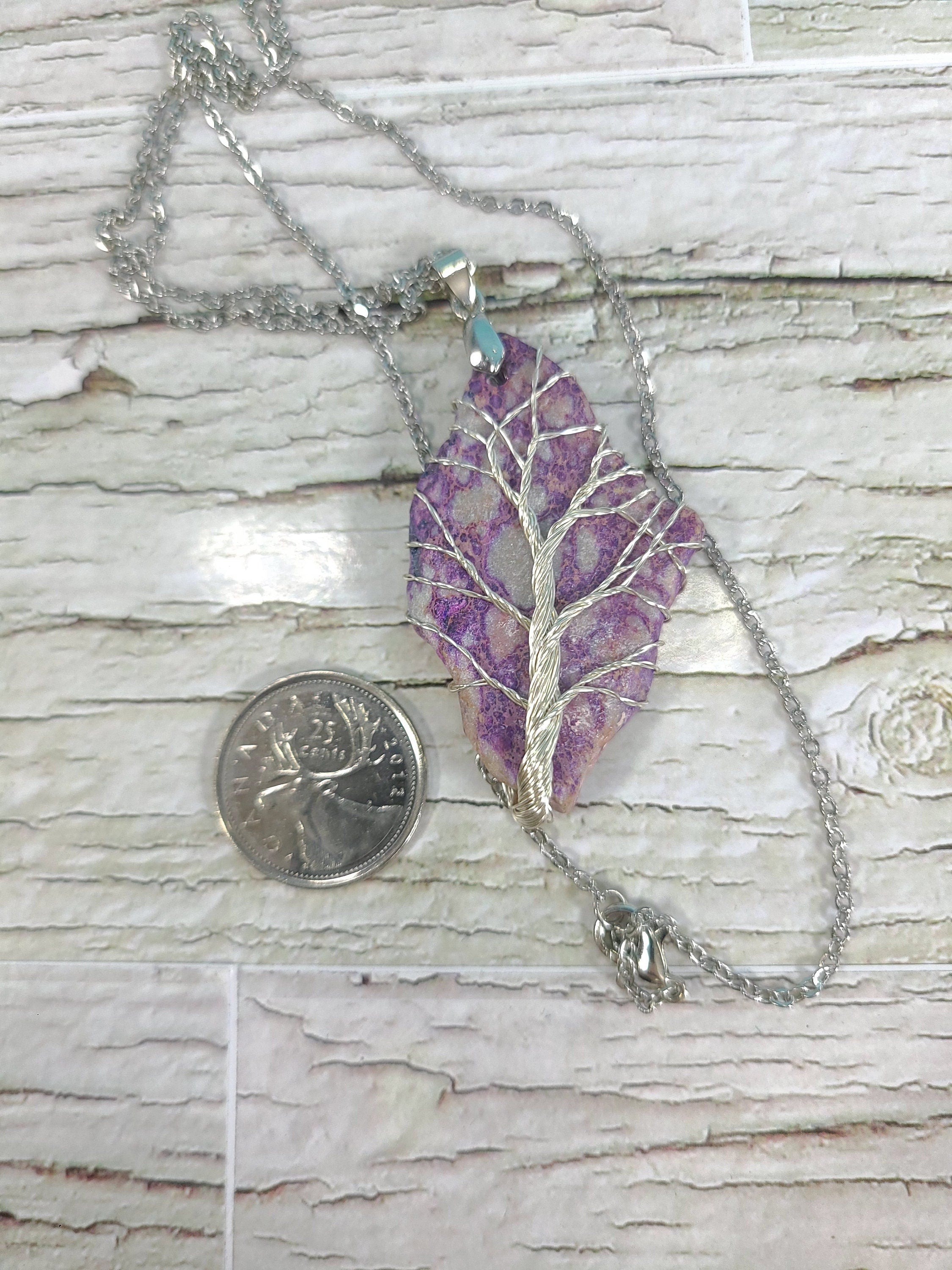 Purple tree-shaped pendant on a chain with a quarter for scale on a wooden surface