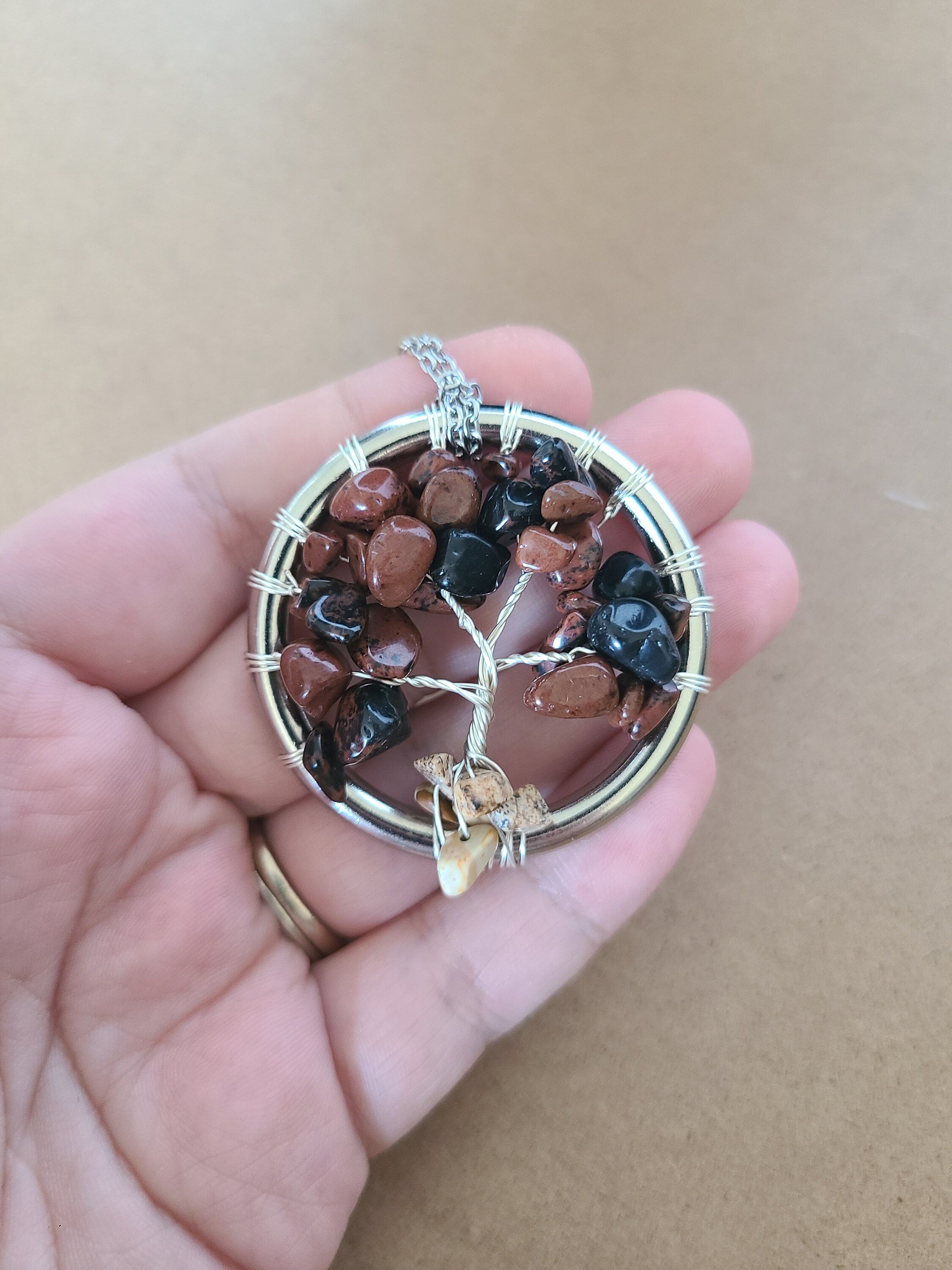 Tree of Life pendant with stones held in a hand against a beige background