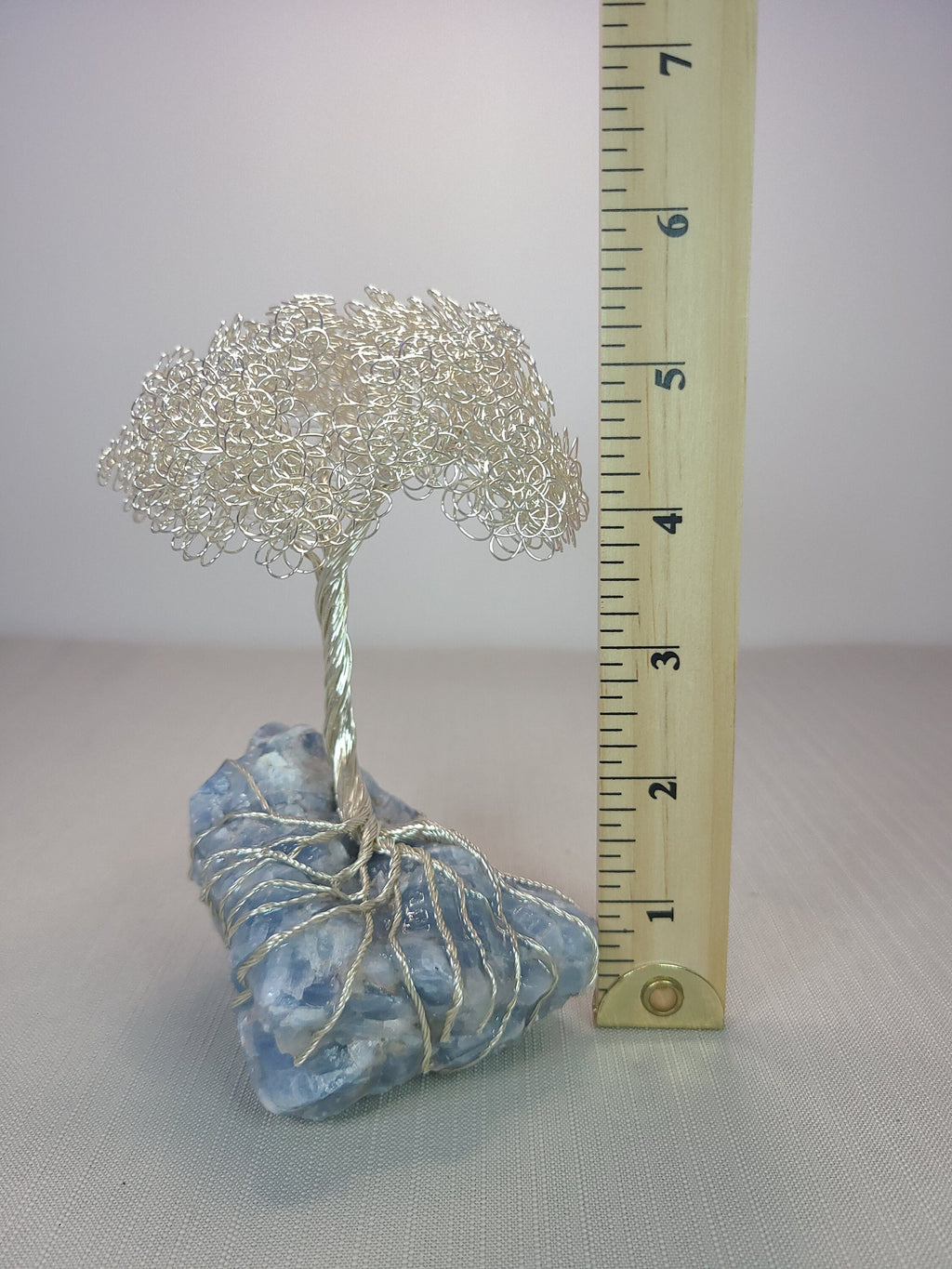Small silver tree on a blue stone with a ruler for scale on a white background