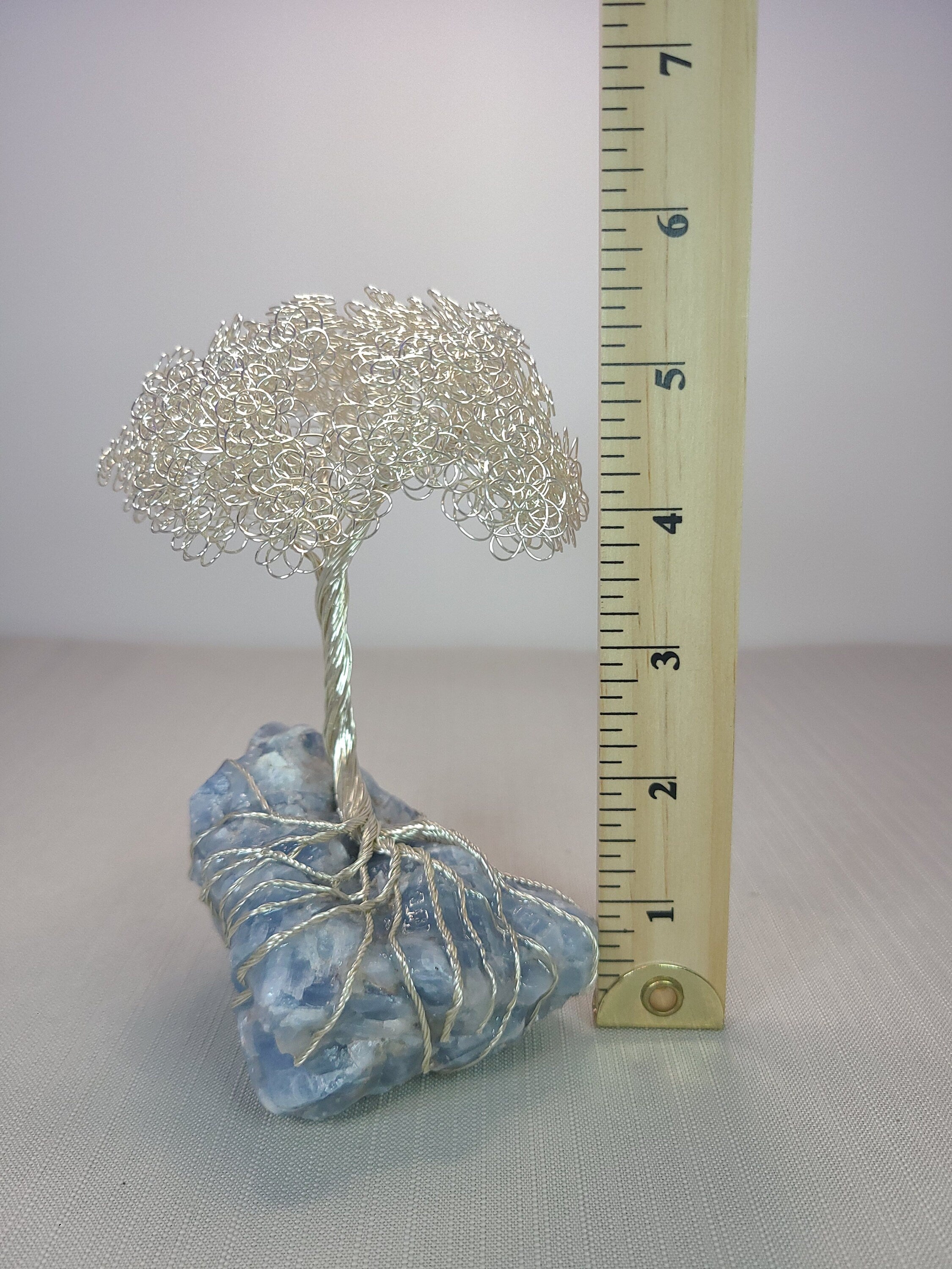 Small silver tree on a blue stone with a ruler for scale on a white background