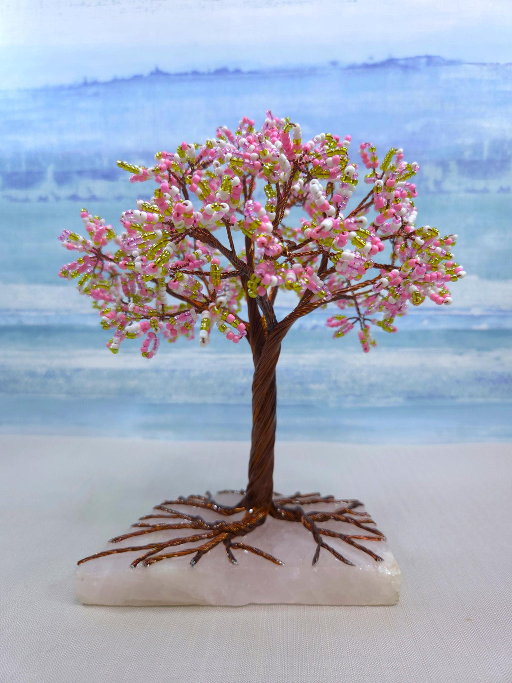 Decorative tree with pink blossoms on a white base against a blurred landscape background
