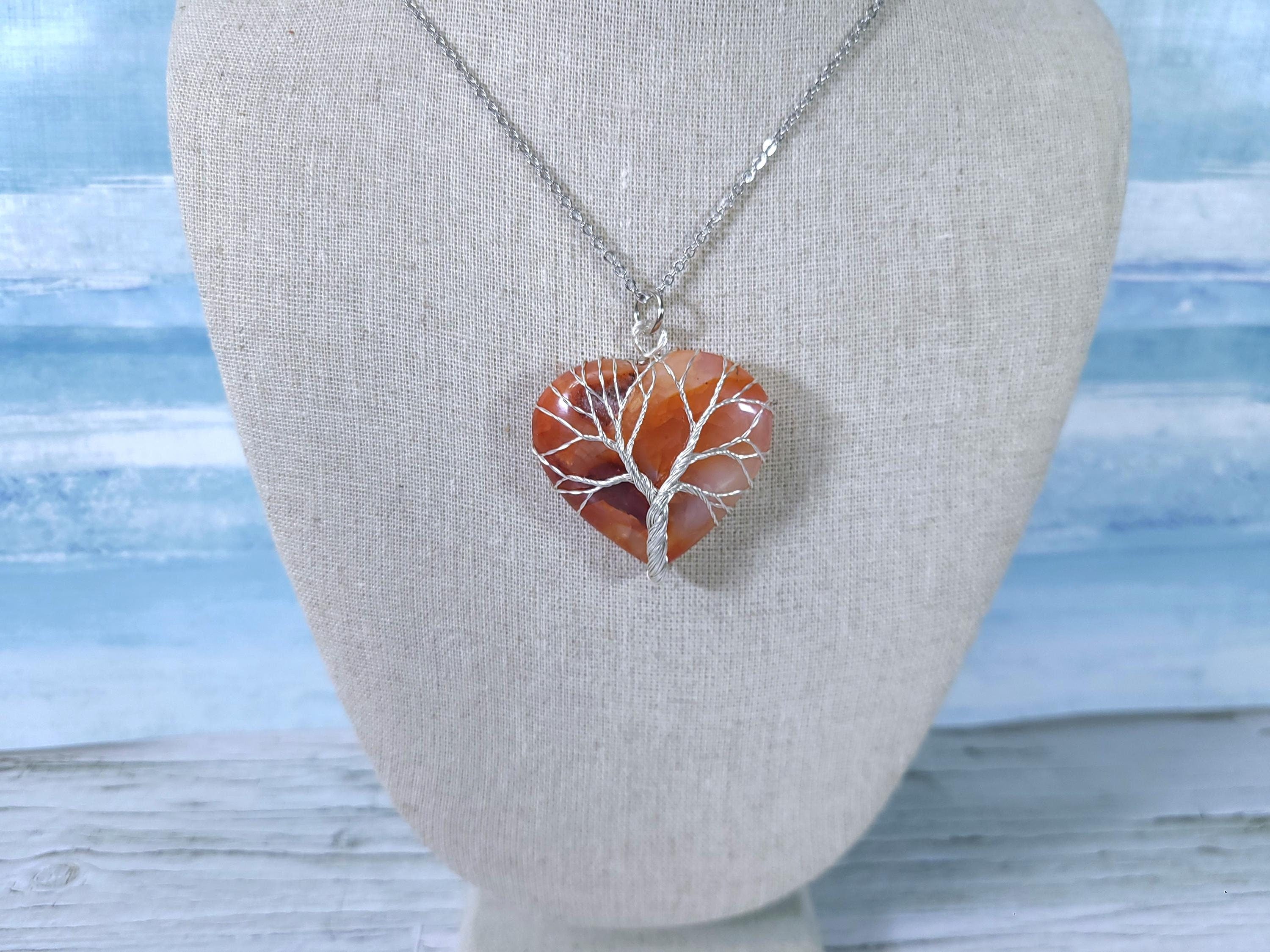 Heart-shaped pendant with tree design on a mannequin bust against a light background