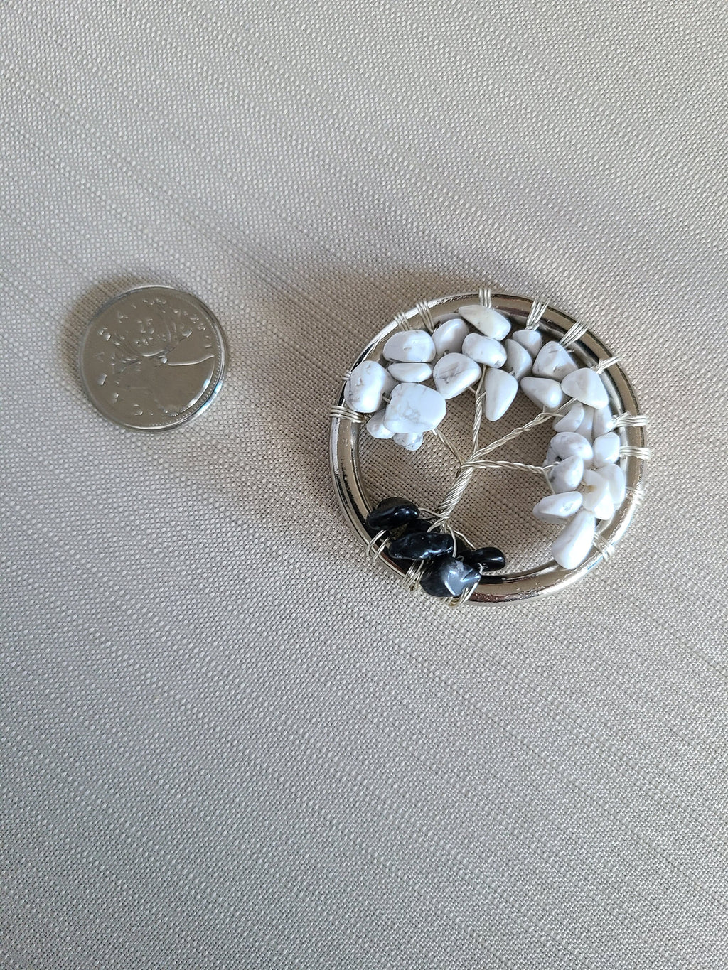 Small decorative item with pebbles resembling a tree of life on a light gray background, next to a coin for scale.