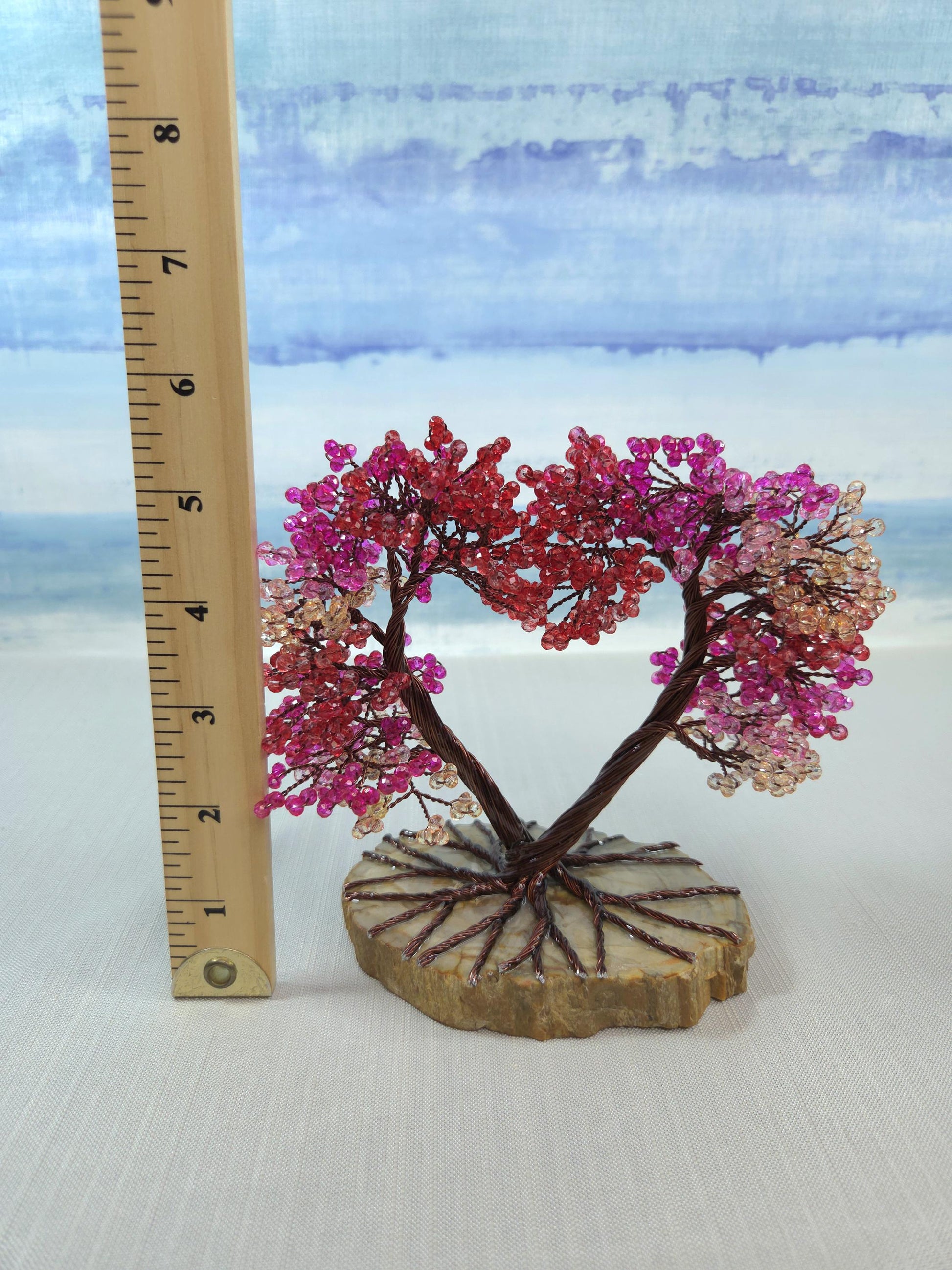 Decorative tree with pink and red beads on a stone base next to a ruler for scale.