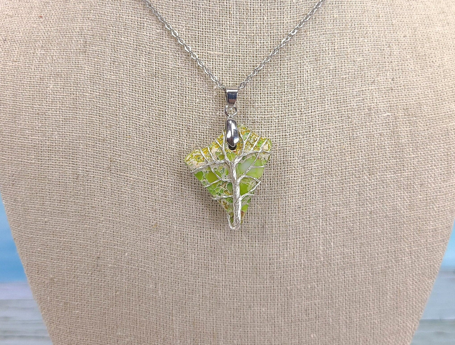Green leaf-shaped pendant on a silver chain against a beige background