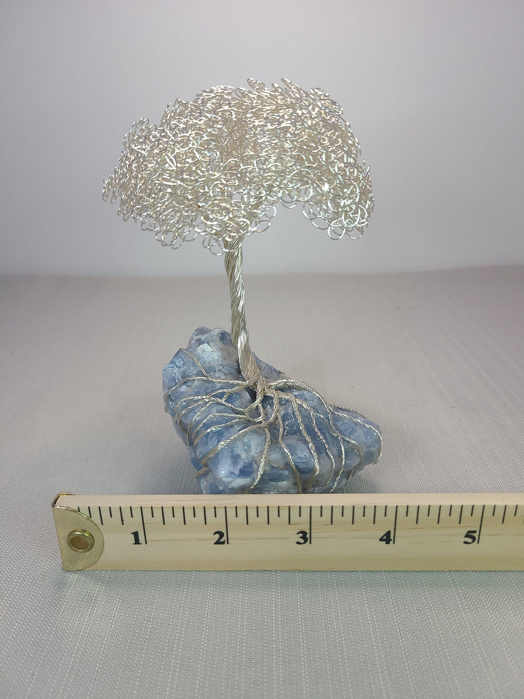 Decorative wire tree on a rock with a ruler for scale against a plain background