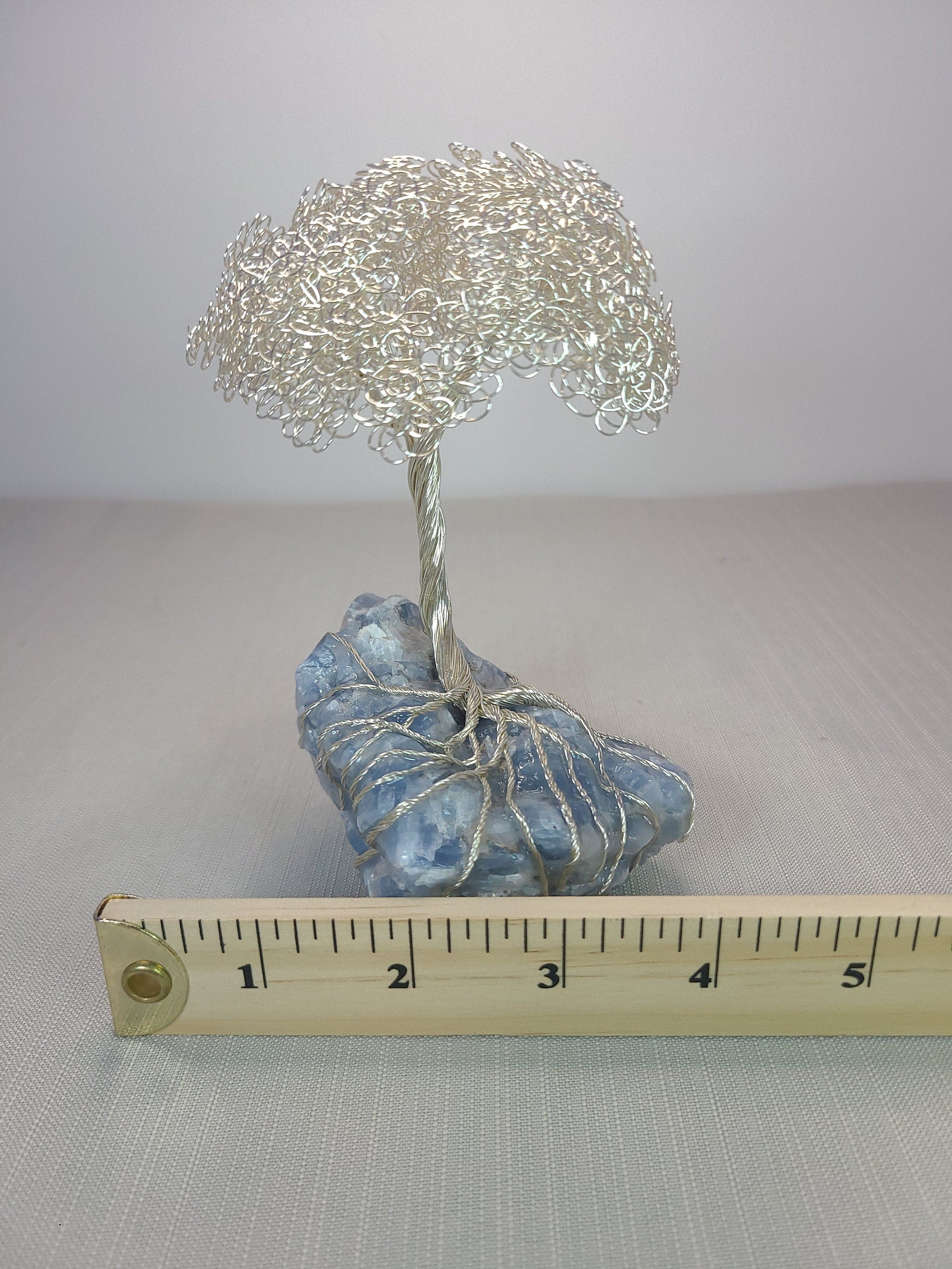 Decorative wire tree on a rock with a ruler for scale against a plain background