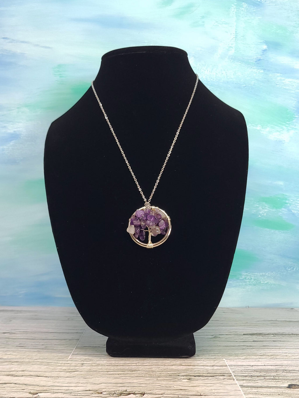 Necklace with a purple pendant on a black bust against a light blue watercolor background