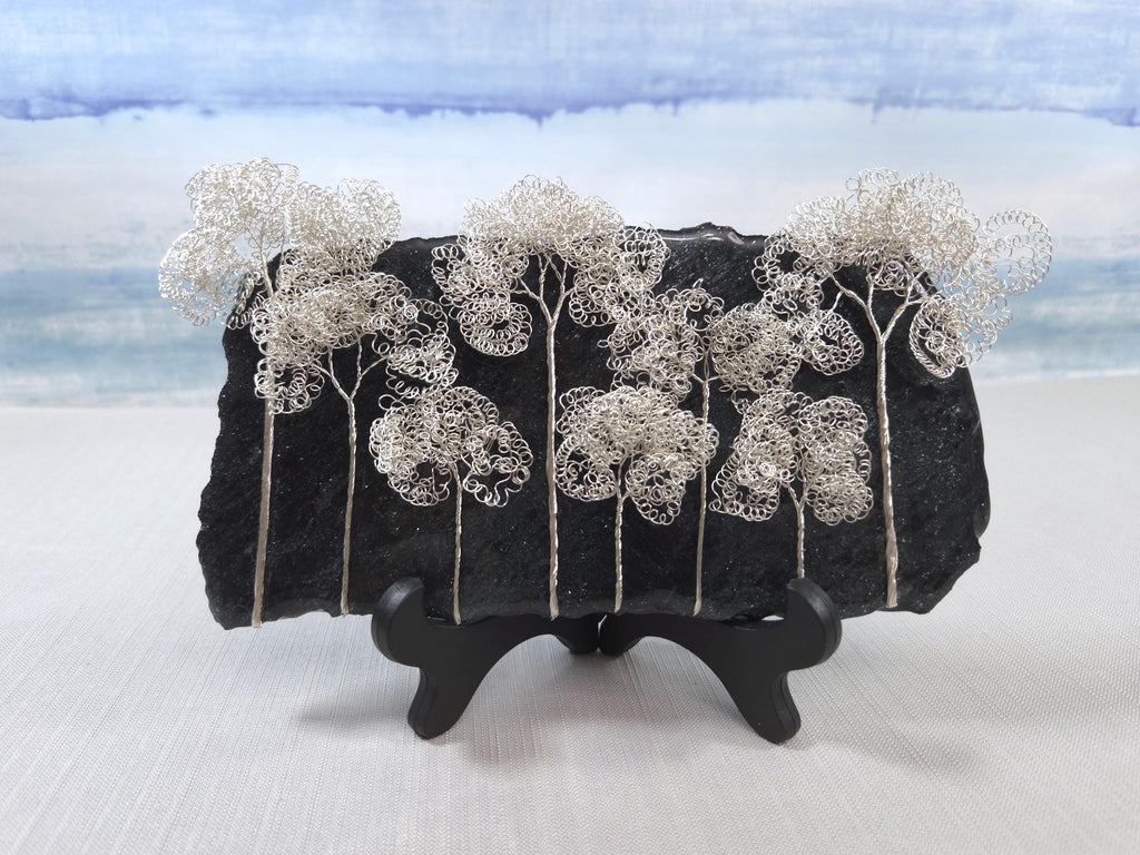 Decorative piece with wire trees on a black base against a light blue sky.