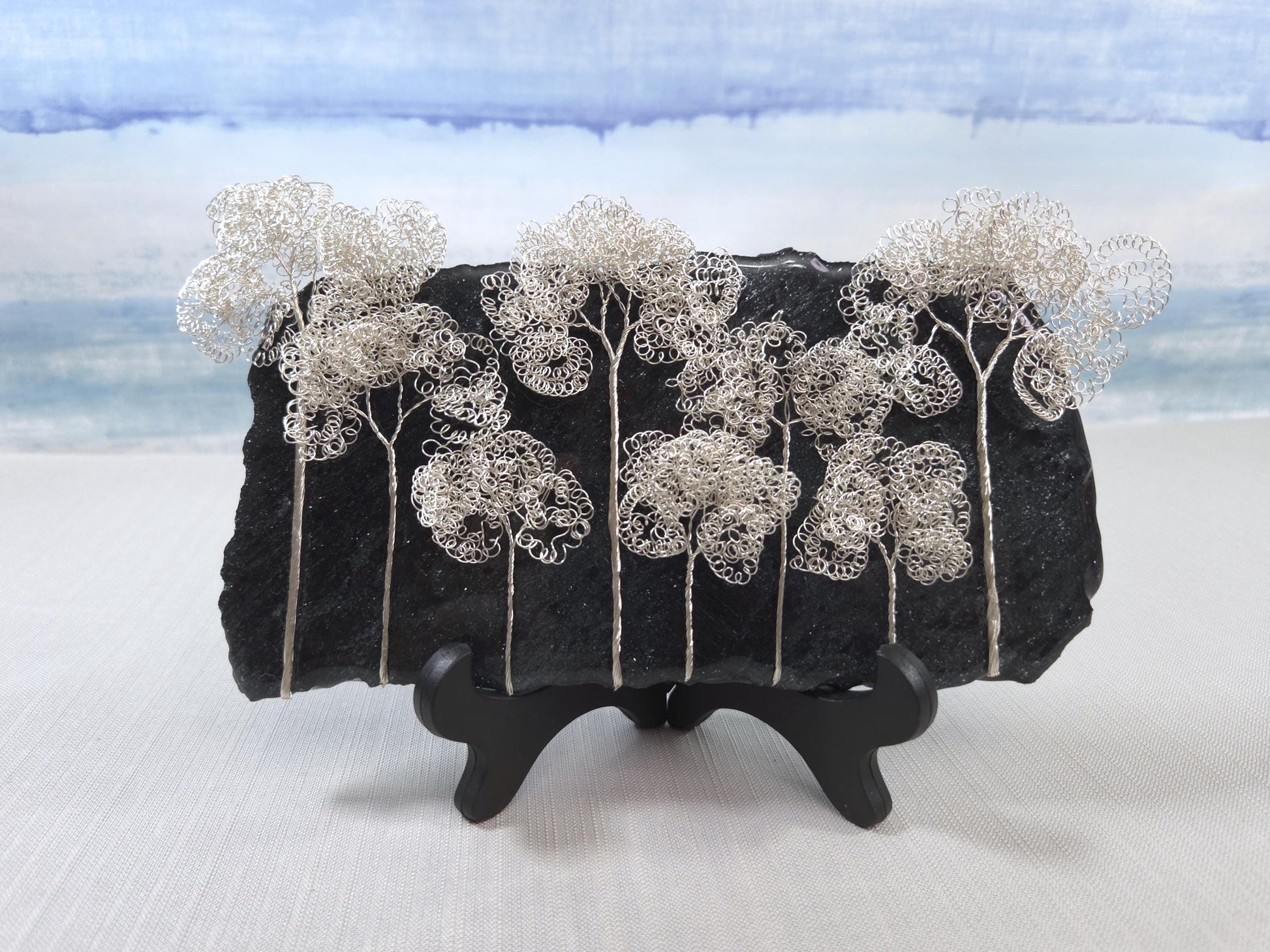Decorative piece with wire trees on a black base against a light blue sky.