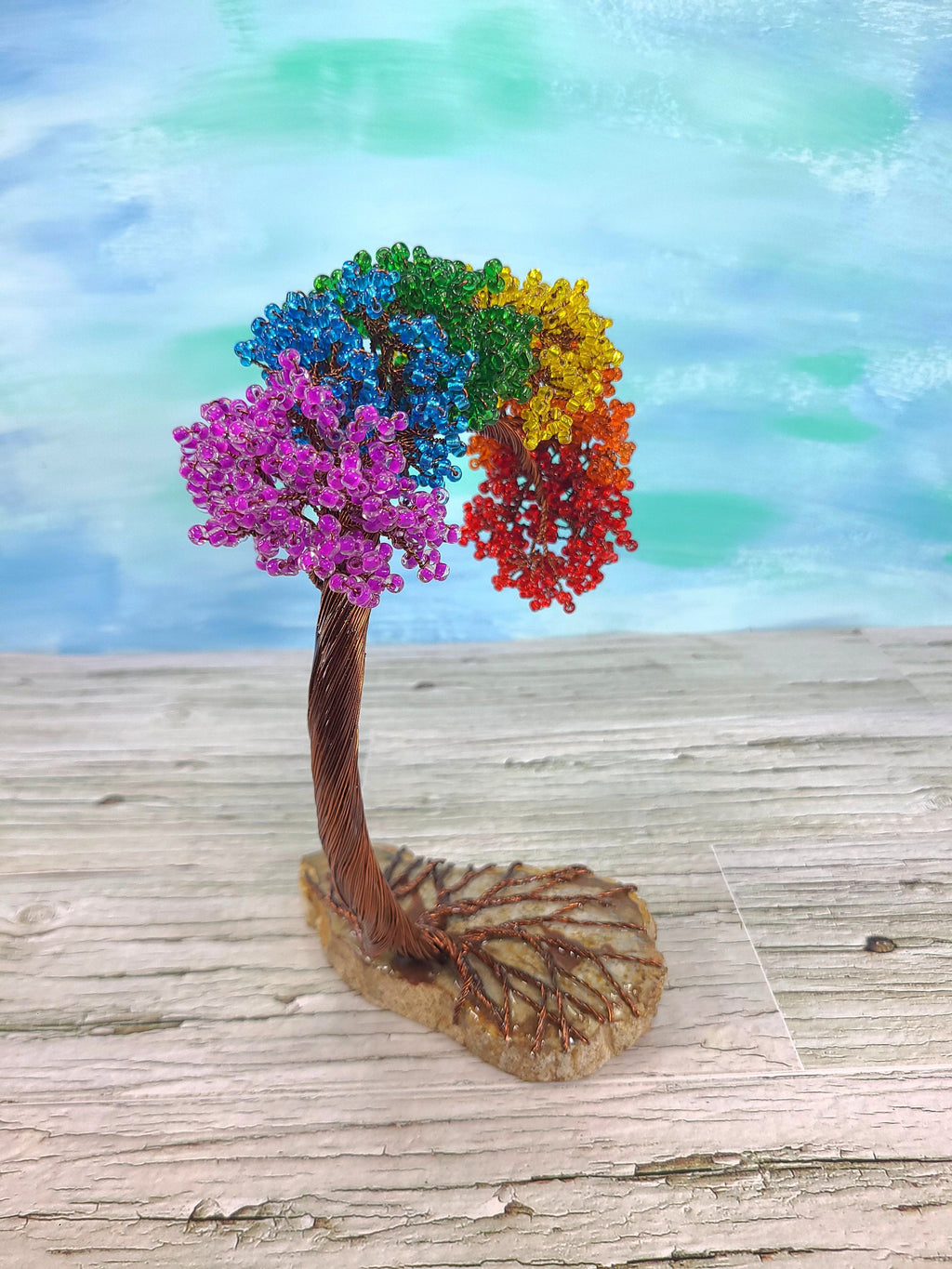 Colorful tree figurine with rainbow-colored leaves on a wooden surface with a watercolor background.