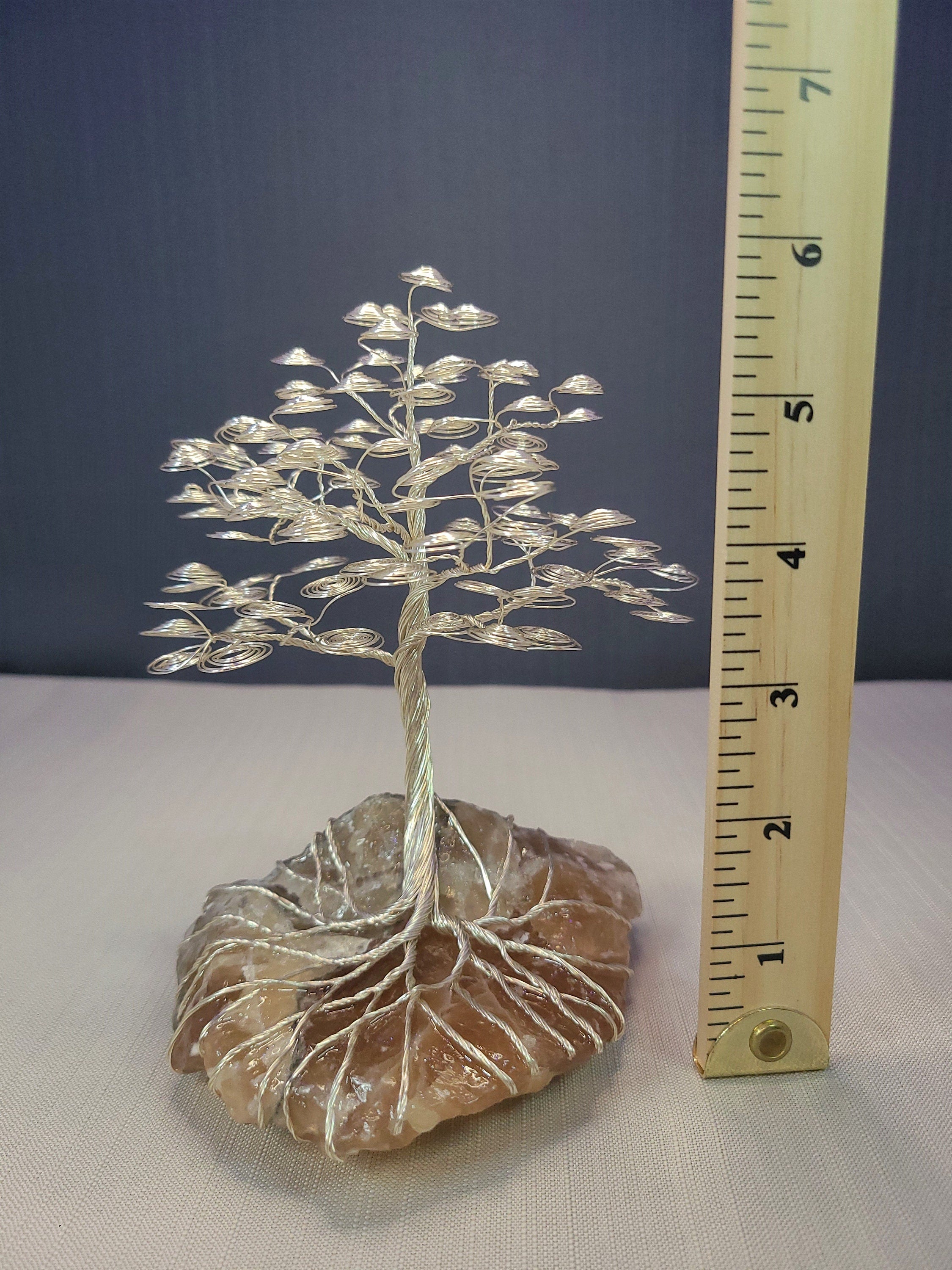 Wire tree sculpture on a rock with a ruler for scale against a dark blue background