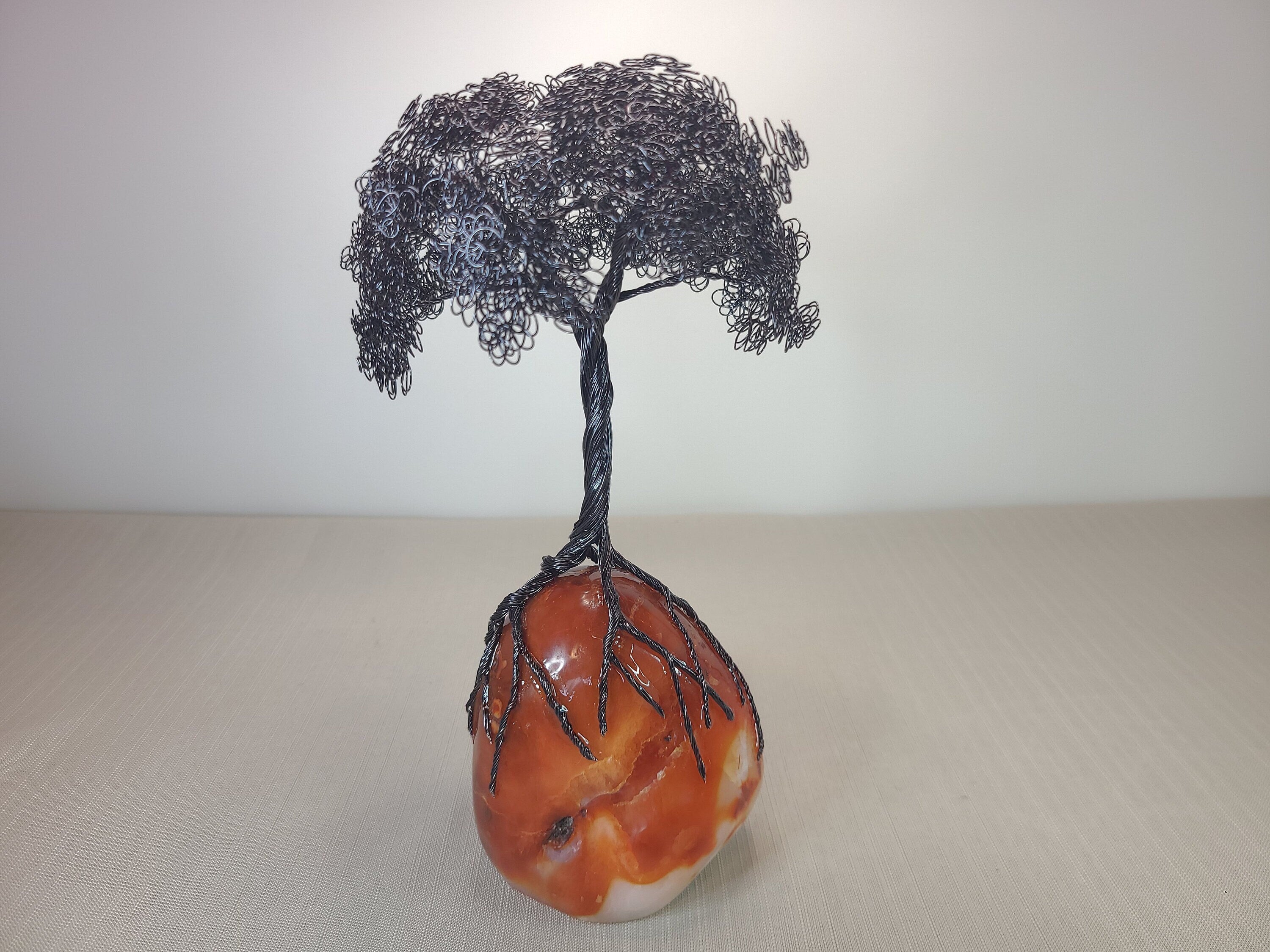Wire tree sculpture on a rock with a plain background