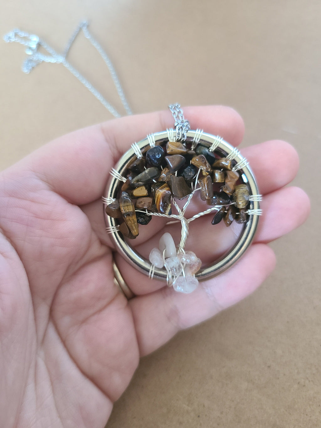 Hand holding a tree of life pendant with stones and wirework against a beige background