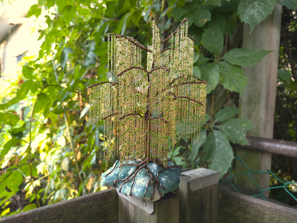 Decorative metal tree sculpture on a wooden post with greenery in the background