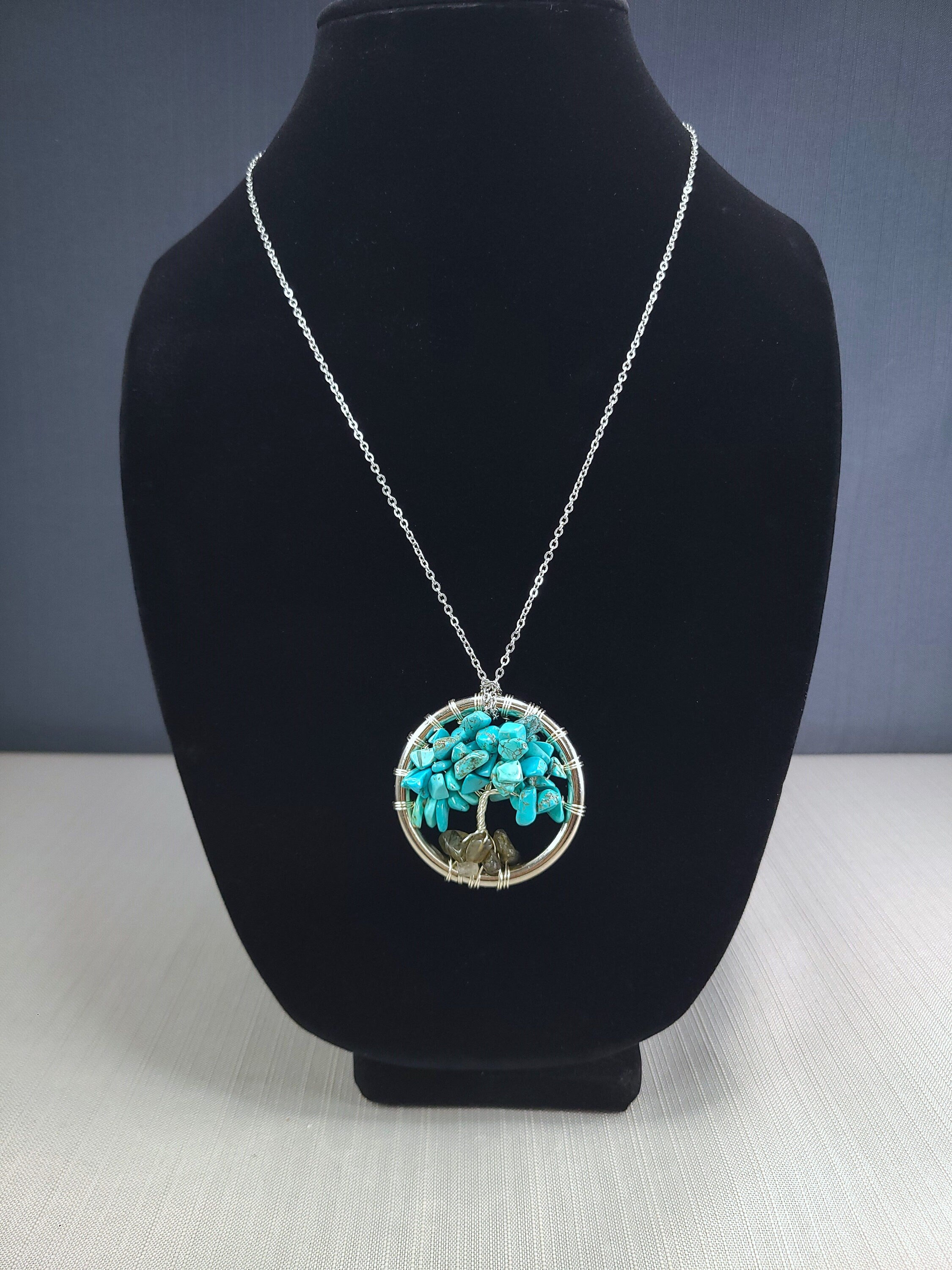 Necklace with a turquoise pendant on a black bust against a gray background