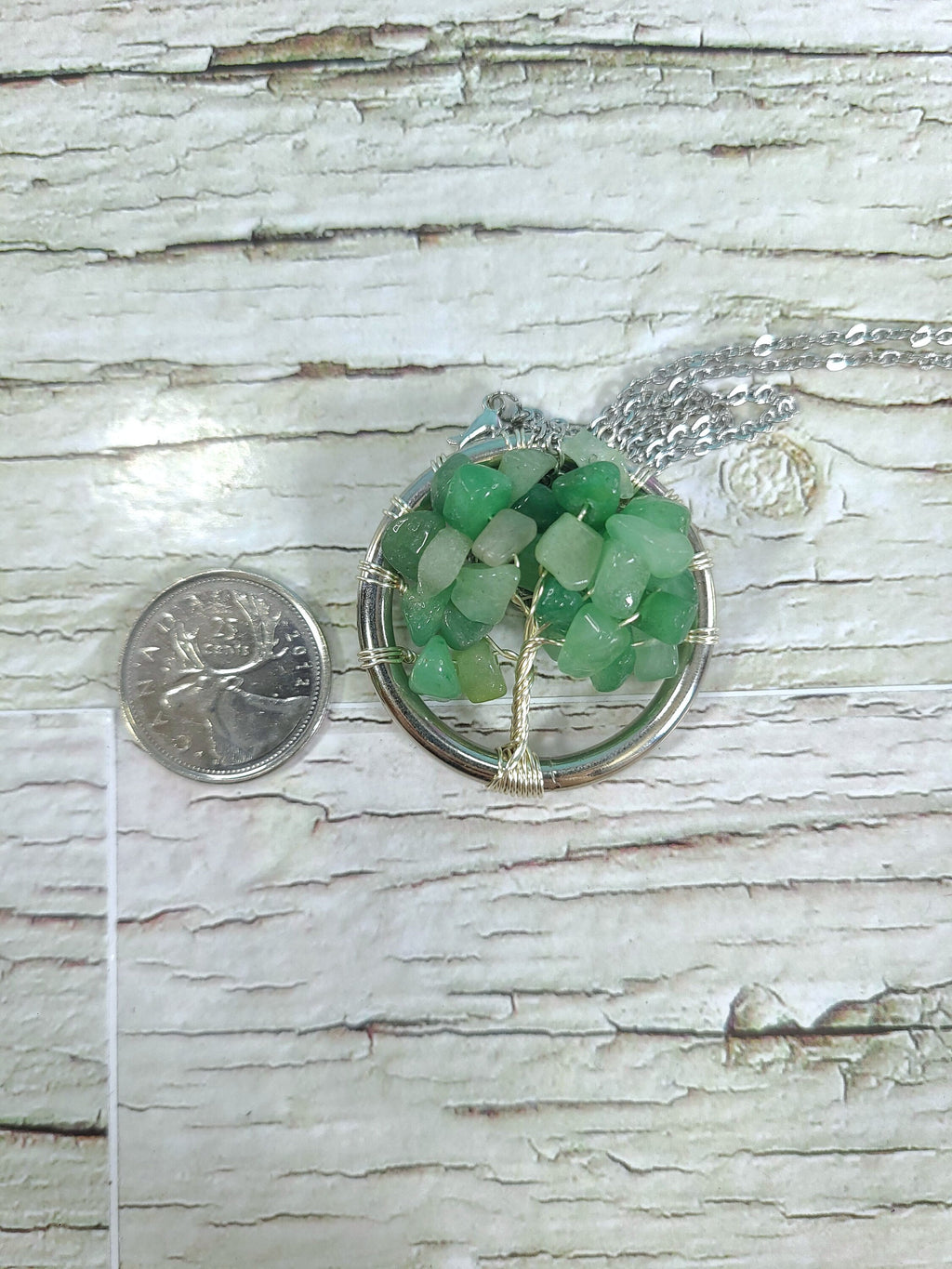 Green sea glass necklace on a wooden surface with a coin for scale